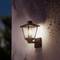 Lanterne extérieure fixée à un mur, un soir ou au crépuscule. La lampe dégage une lumière chaleureuse et illumine les alentours.