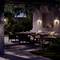 Une terrasse accueillante au crépuscule avec un canapé, une table et des chaises, entourée d'une végétation luxuriante et d'un éclairage doux.