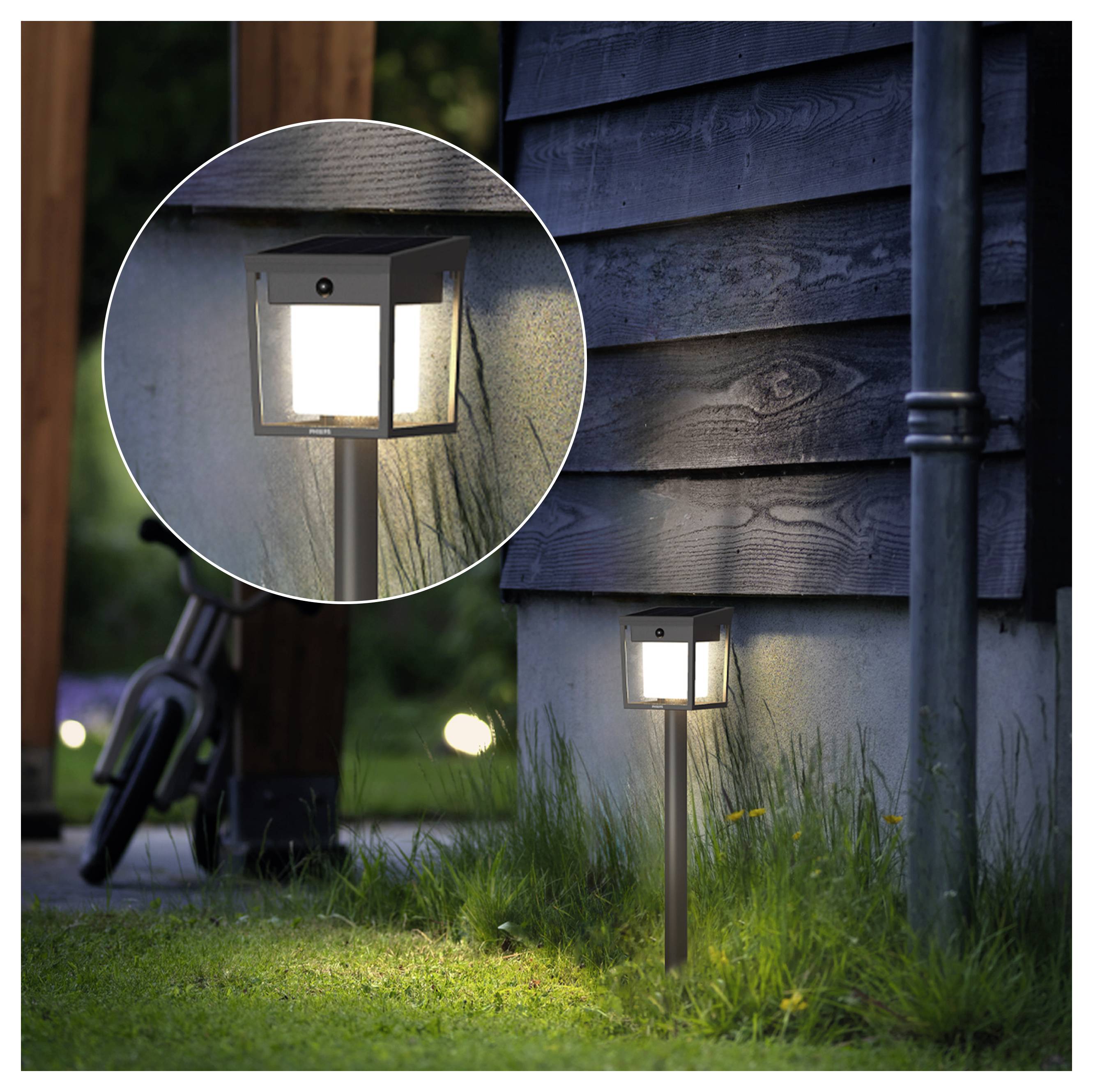Lampadaire de sentier extérieur monté sur un pieu à côté du mur d'une maison, montré allumé au crépuscule avec un gros plan circulaire encadré de la lampe.