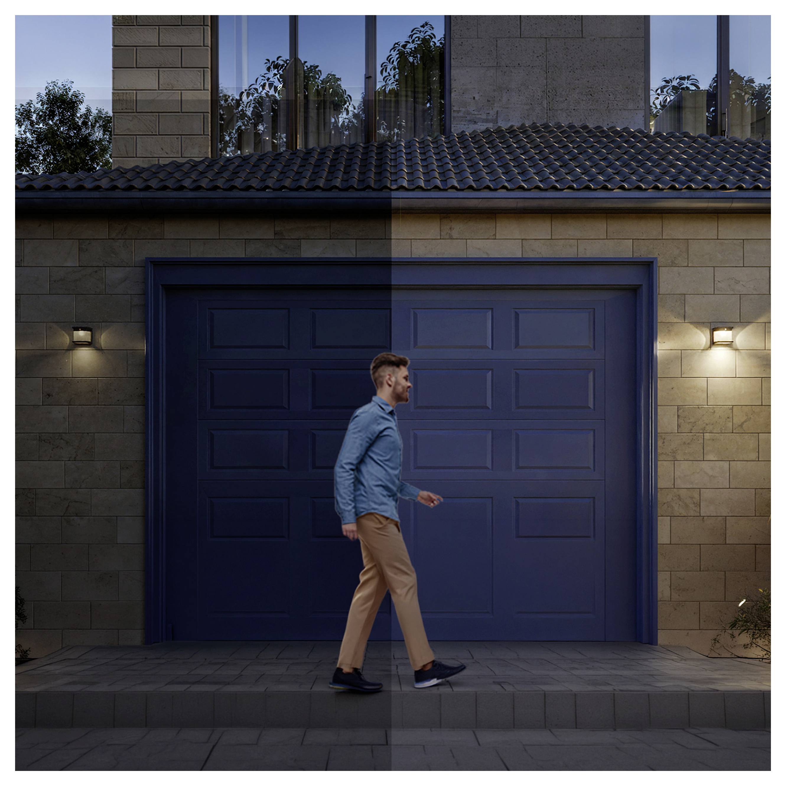 Un homme passant devant une porte de garage bleue fermée au crépuscule à l'extérieur d'une maison moderne.