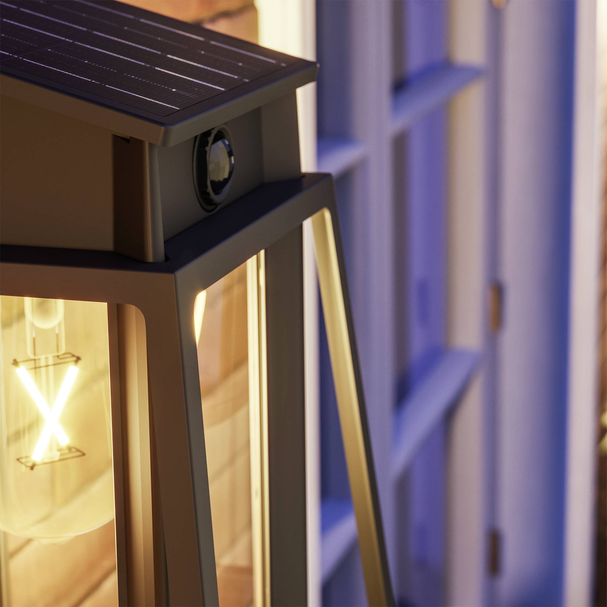 Lanterne avec ampoule, illuminée au crépuscule sur une terrasse. Économe en énergie grâce au panneau solaire situé sur sa partie supérieure.