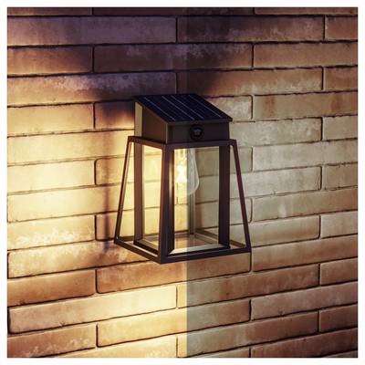 Lanterne murale solaire d'extérieur luisant contre un mur de briques, avec une lumière chaude illuminant un côté.