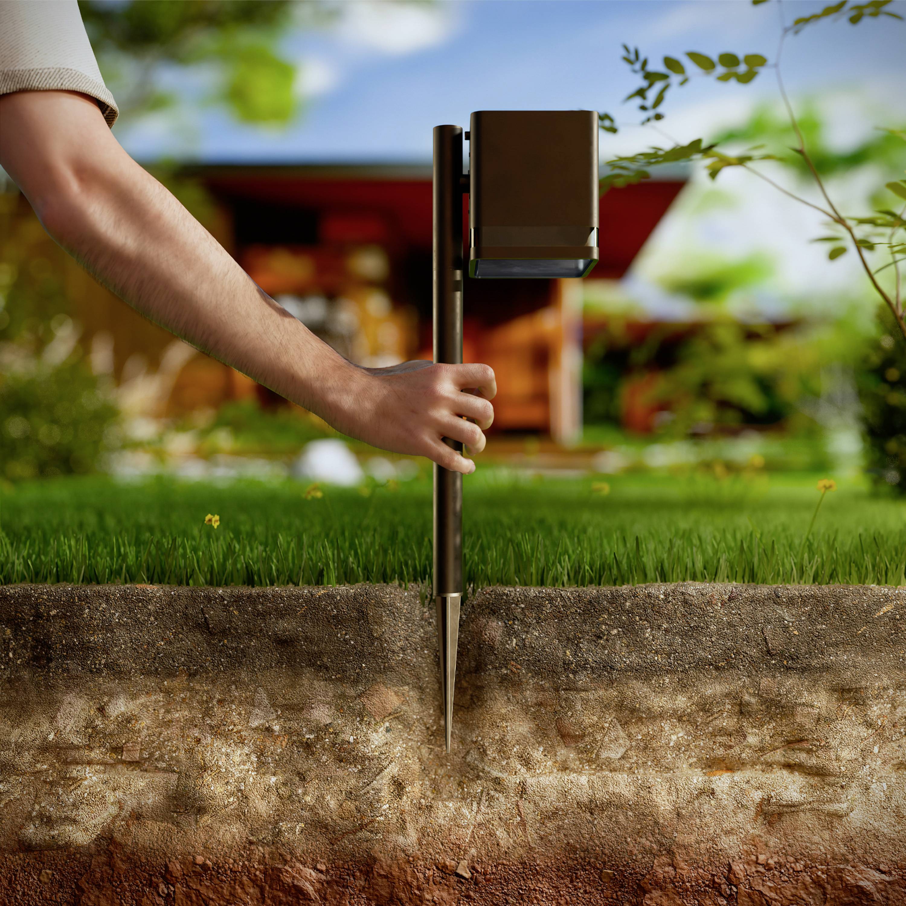 Une main tient un appareil de test de sol fiché dans la terre ; à l'arrière-plan, une maison moderne avec un paysage de jardin.