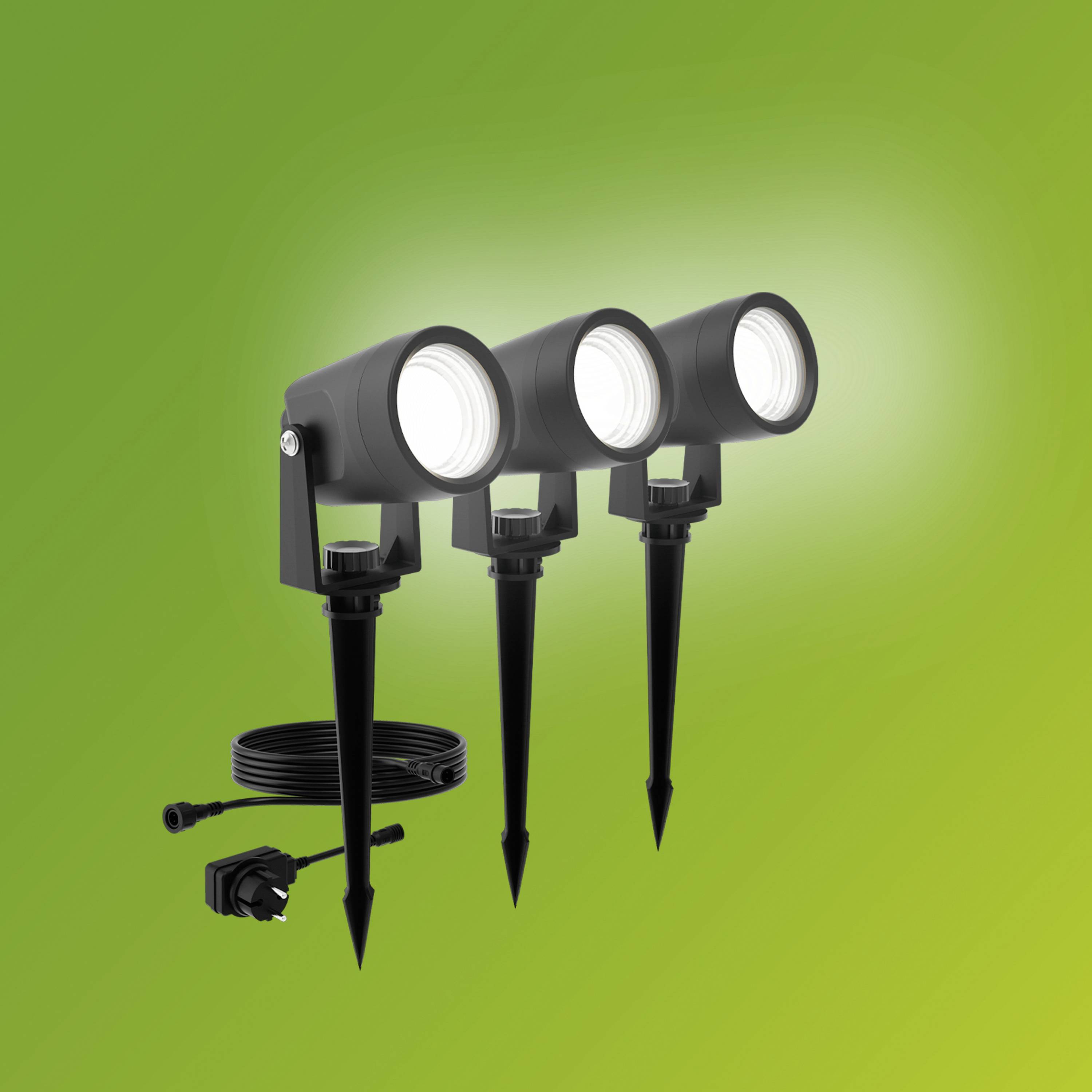 Trois projecteurs noirs extérieurs avec piquets de terre, sur un fond vert. Ils sont connectés à des câbles et éclairent vers l'avant.