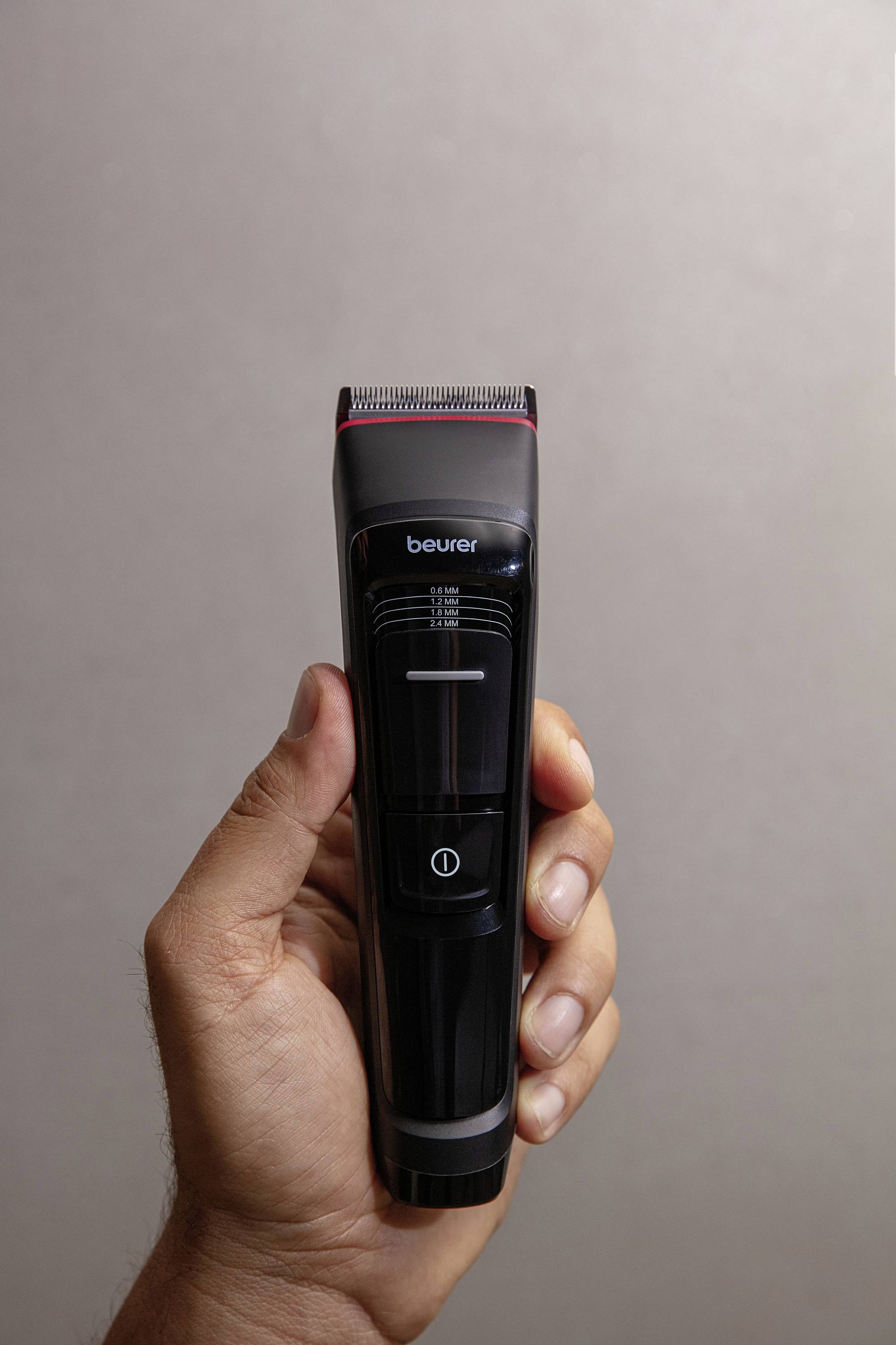 Une main tient une tondeuse électrique noire à la forme élancée, prête à être utilisée.