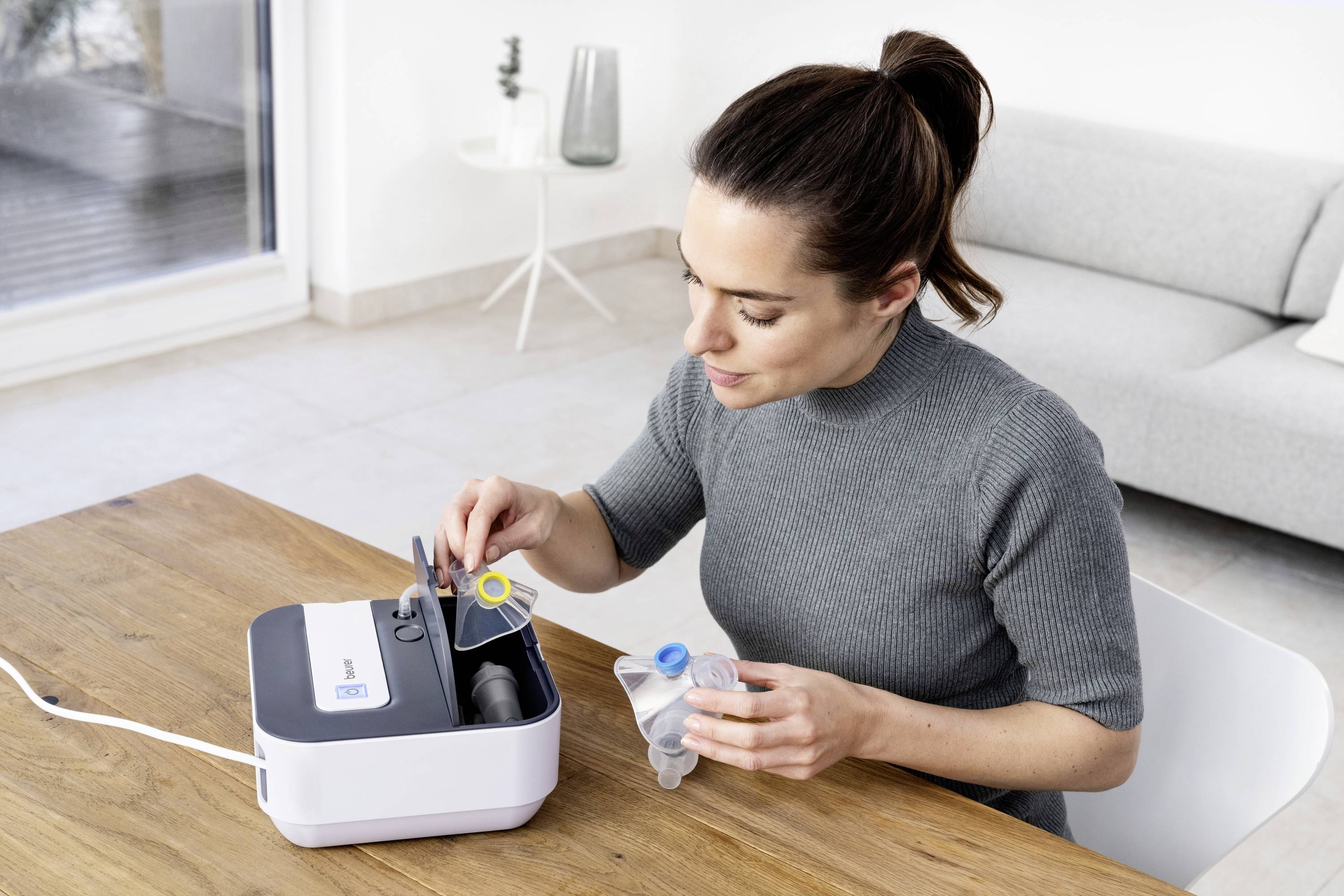 Une personne remplit un appareil de thérapie respiratoire sur une table. Elle tient des pièces de l'appareil à la main, avec un canapé en arrière-plan.