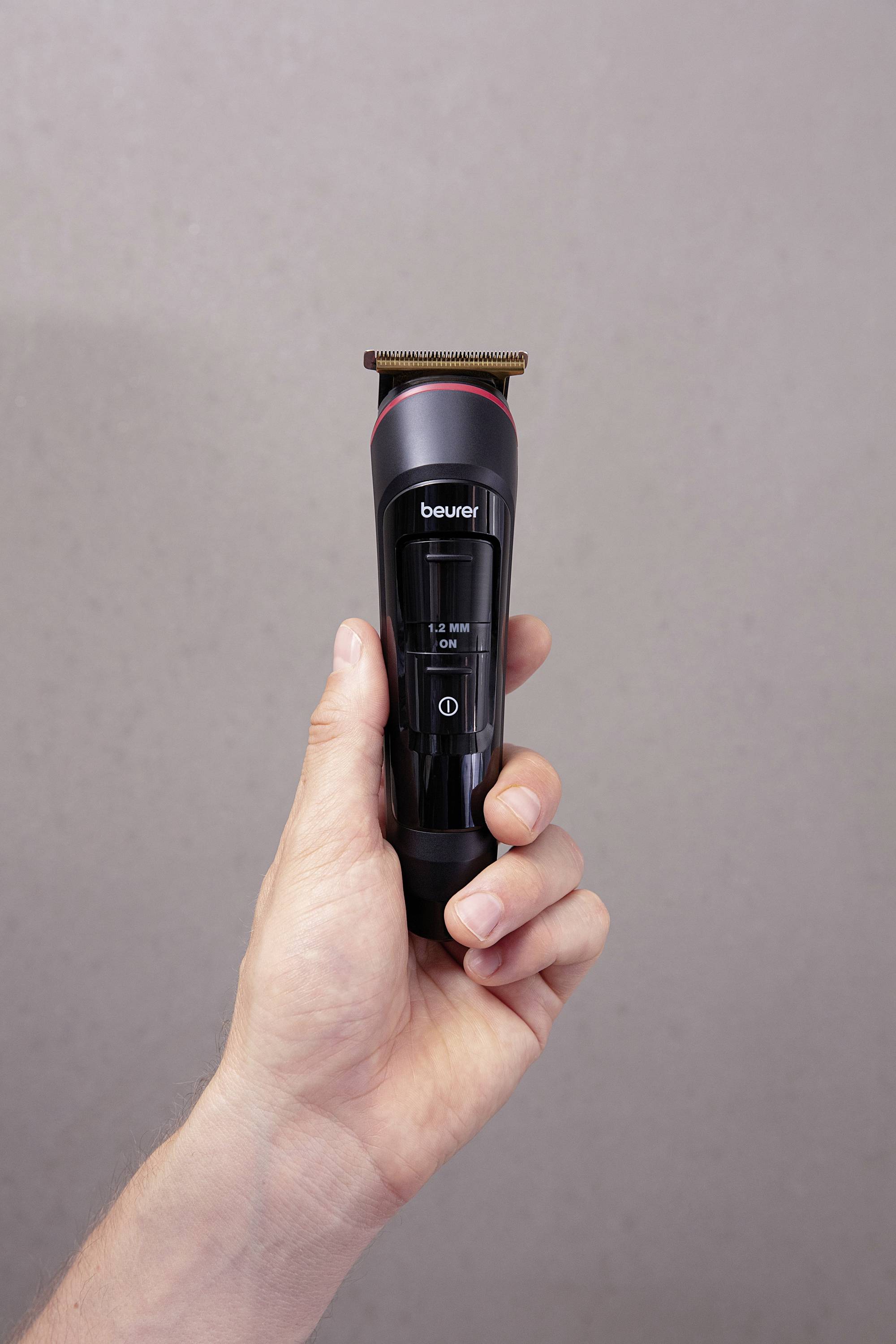 Une main tient un rasoir électrique noir devant un fond gris clair.