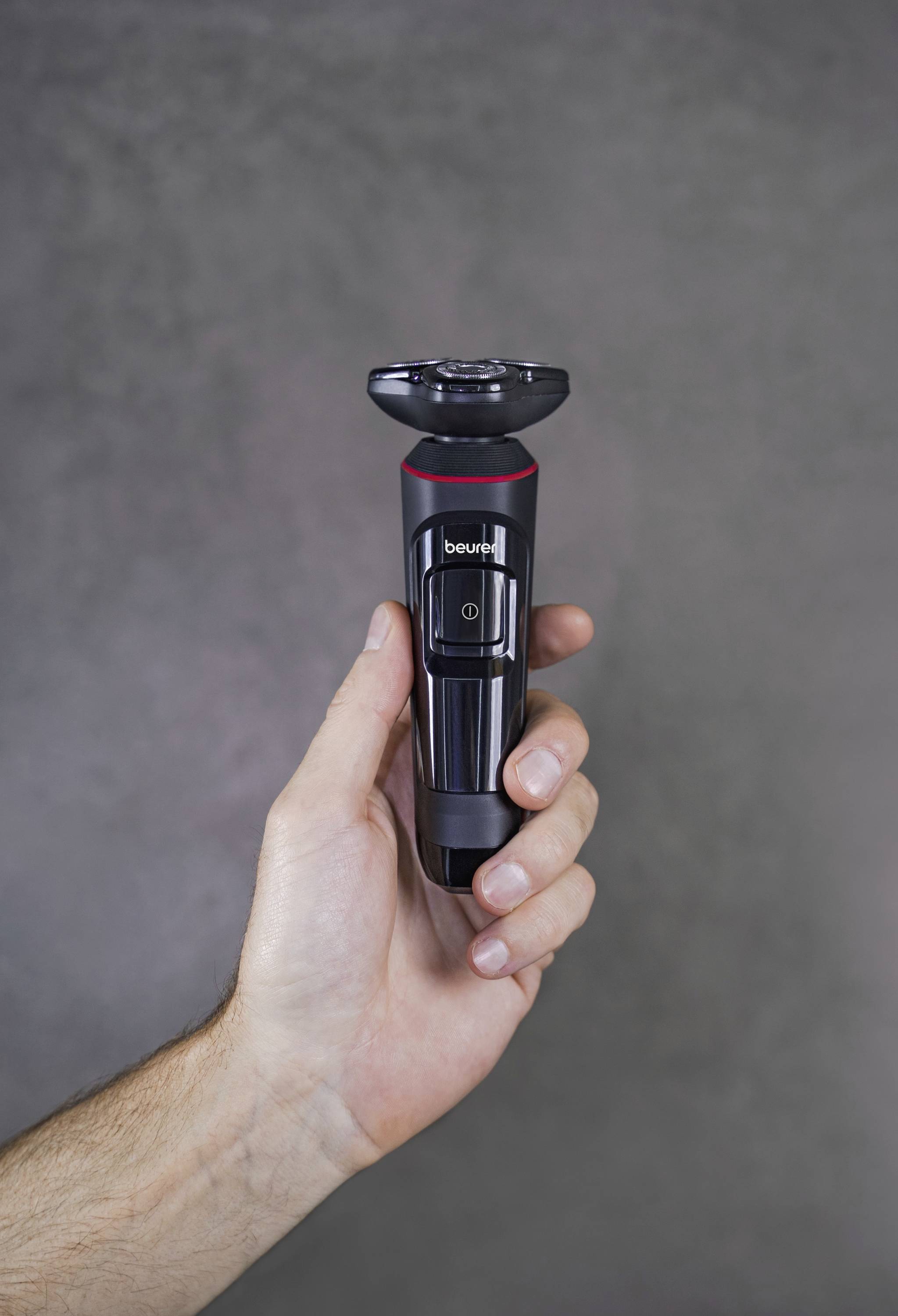 Une main tient un rasoir électrique à boîtier noir sur un fond gris.