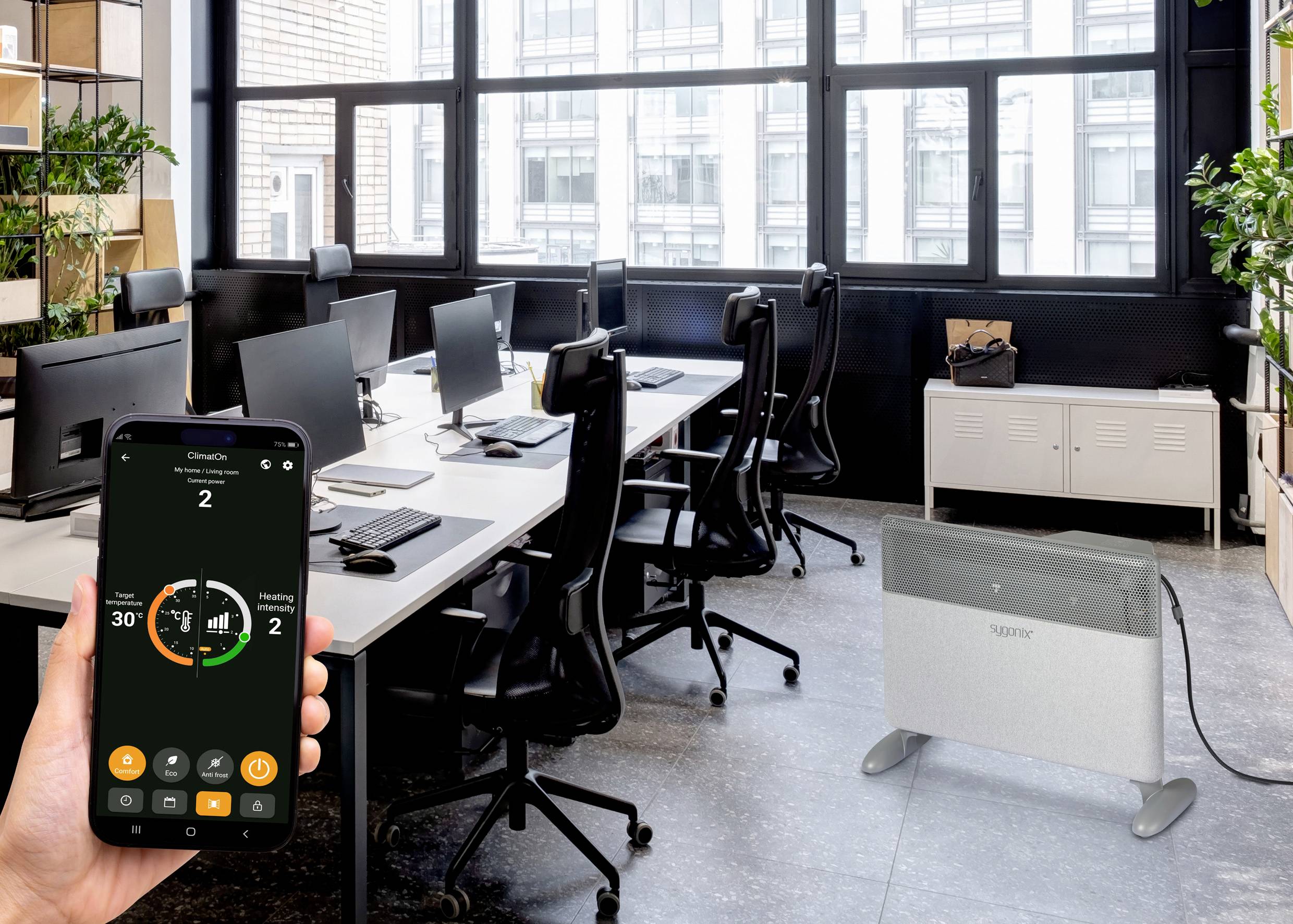 Un smartphone contrôle un radiateur électrique dans un bureau moderne à plan ouvert. L'écran affiche les réglages de chauffage.