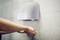 Une personne utilise un sèche-mains mural étiqueté « Drying Master » de SUGOMIX, installé dans un environnement de salle de bain aux murs carrelés.