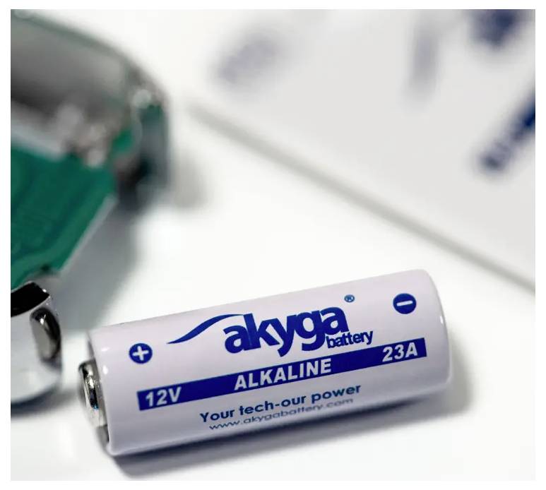 Batterie d'accumulateur portant l'inscription « akyga battery 12V ALKALINE 23A Your tech-our power www.akyga.com » posée sur une table.