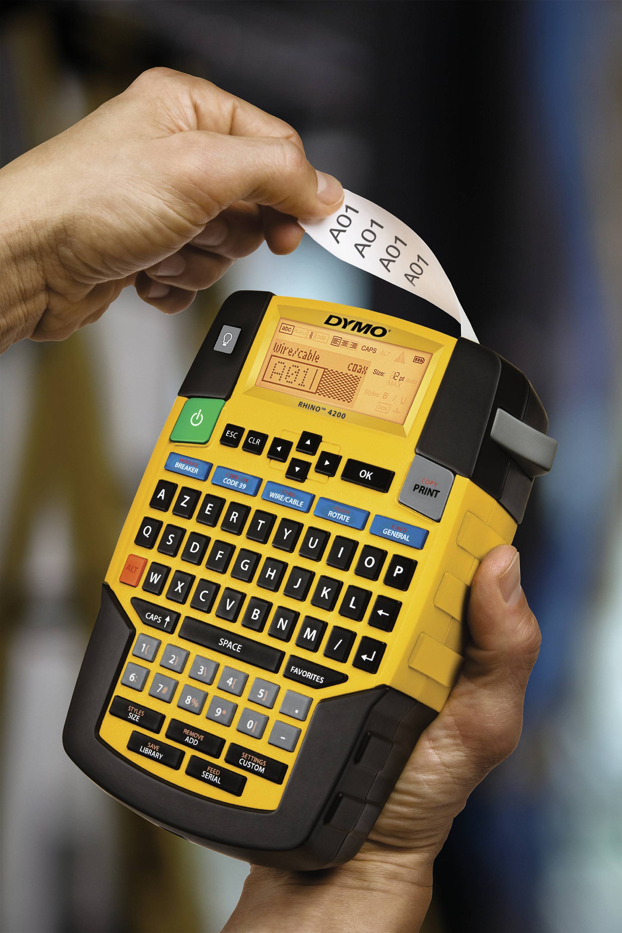 Quelqu'un tient un appareil portable d'étiquetage qui imprime une étiquette avec le texte 'A01'. L'appareil est équipé d'un clavier et d'un écran.
