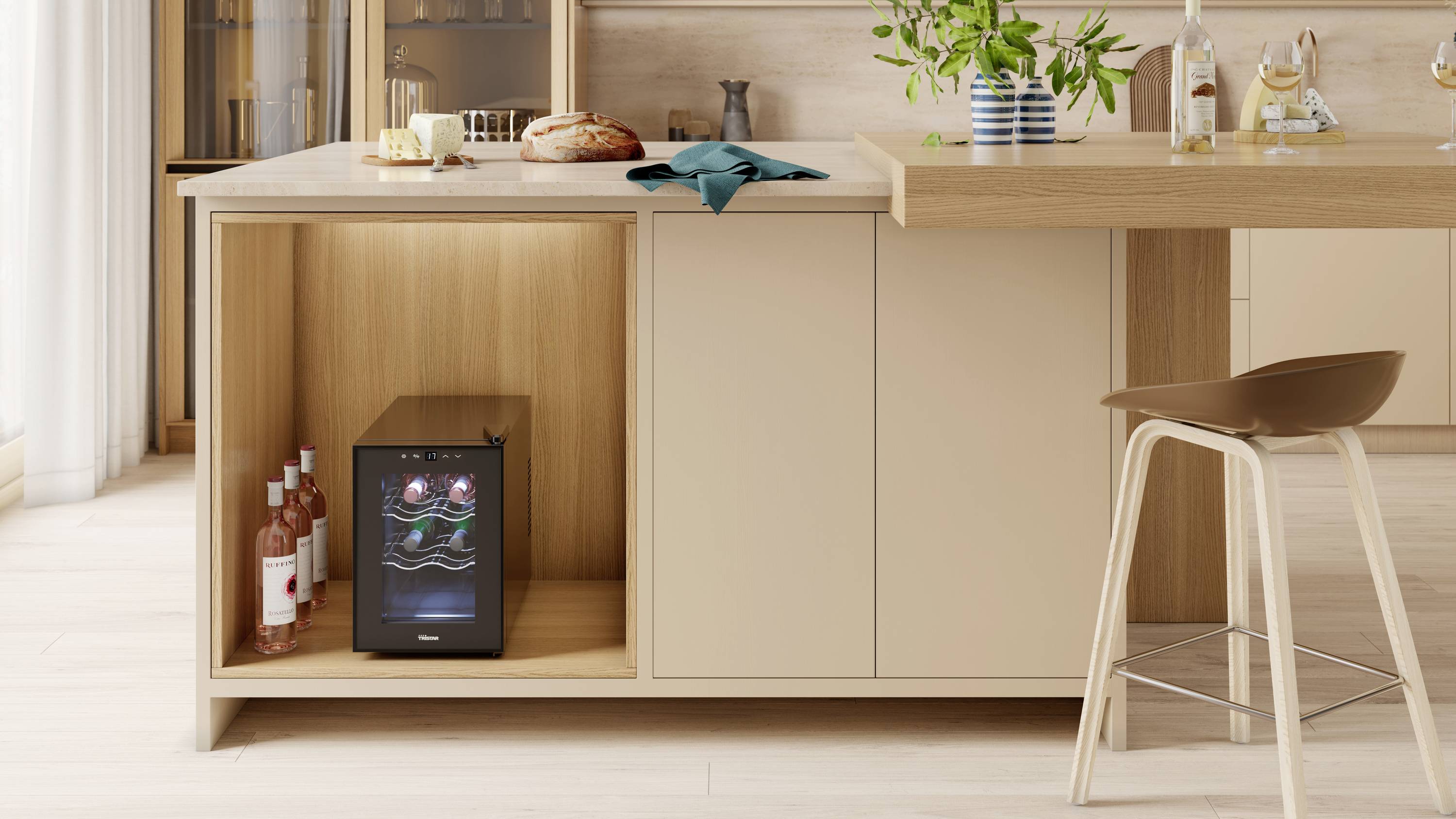 Cuisine avec un comptoir garni de pain, de fromage et de vin. Sous le comptoir, un mini-réfrigérateur à vin contenant plusieurs bouteilles. Un tabouret à droite.