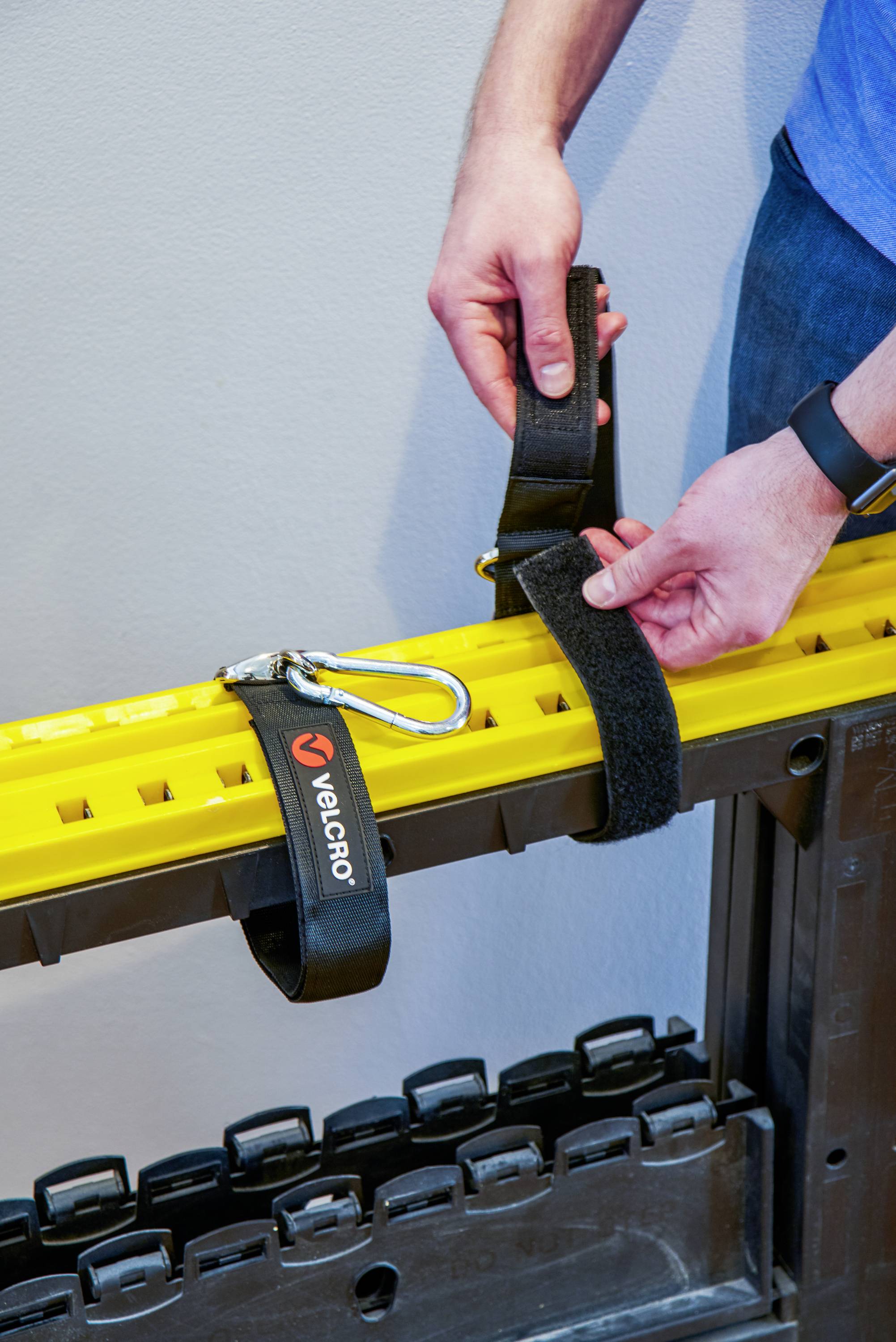 Une personne fixe une bande velcro noire sur un rail jaune. La bande porte un petit logo "Velcro".