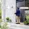 Homme à la porte d'entrée, tenant un colis. La caméra avec module vocal dit : « Bonjour, veuillez déposer le petit colis devant la porte. Merci beaucoup ».