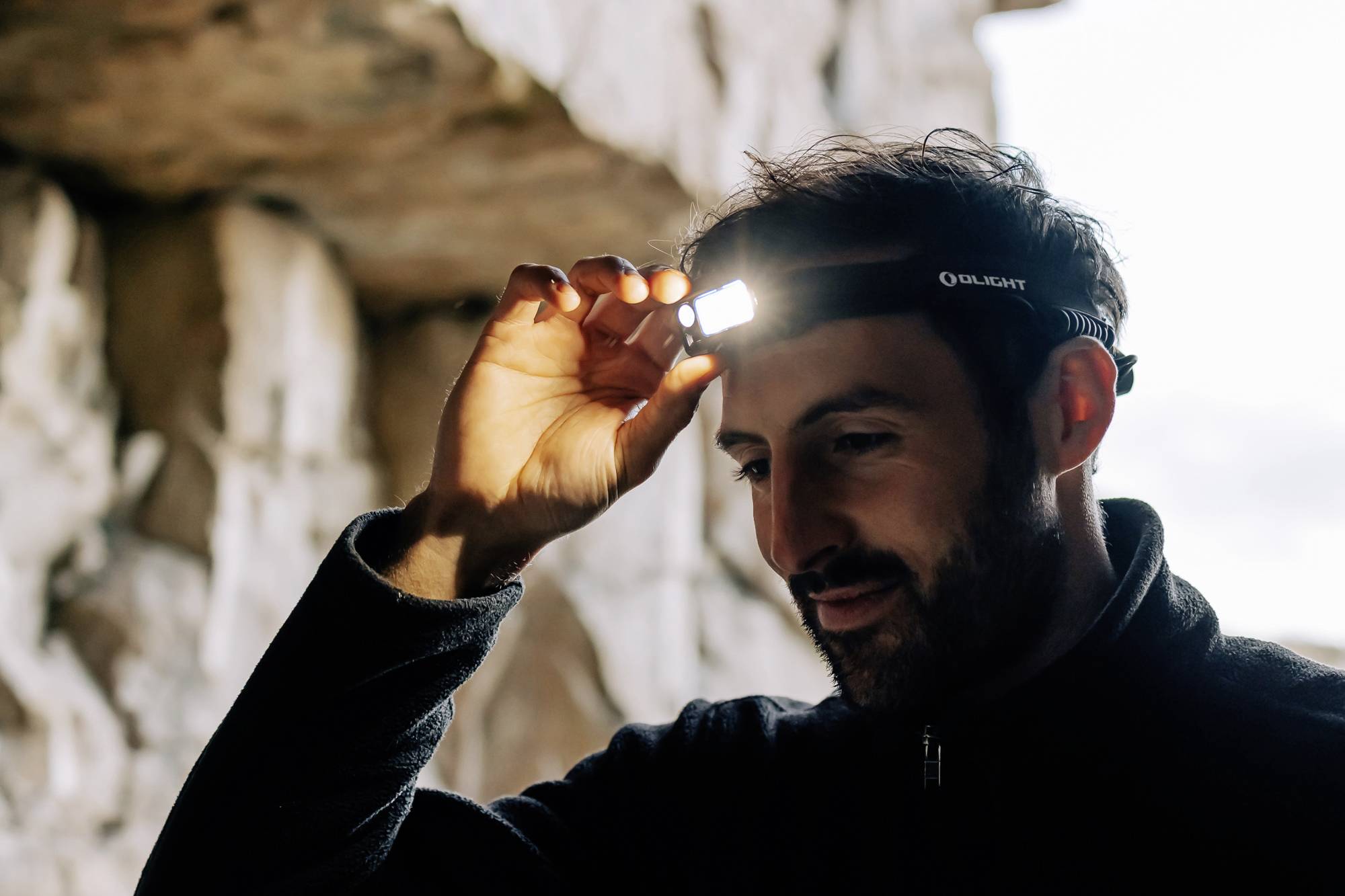 Une personne porte une lampe frontale dans une grotte, illuminant son visage d'une lumière douce pour mieux voir son environnement.