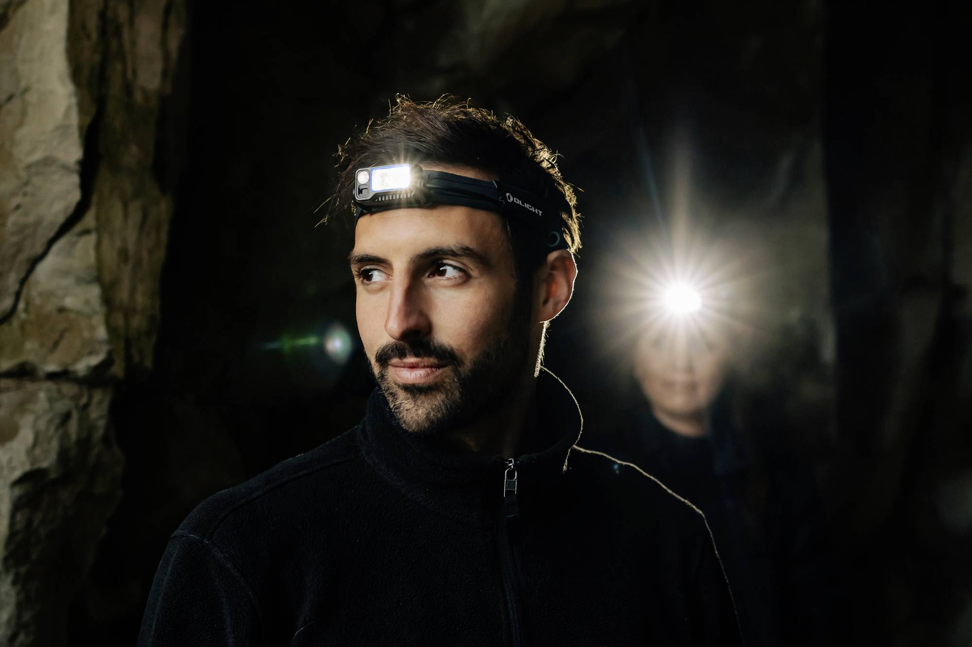 Un homme portant une lampe frontale se tient dans une grotte, une autre personne avec une lampe frontale allumée se trouve en arrière-plan.