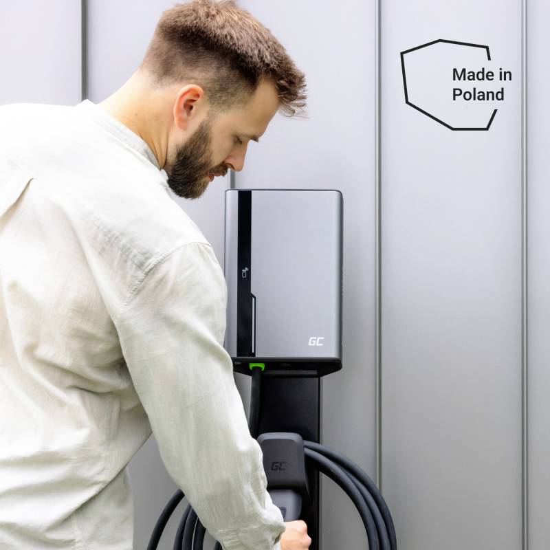 Un homme utilise une station de recharge pour véhicules électriques, et sur le mur se trouve un panneau indiquant 'Made in Poland'.
