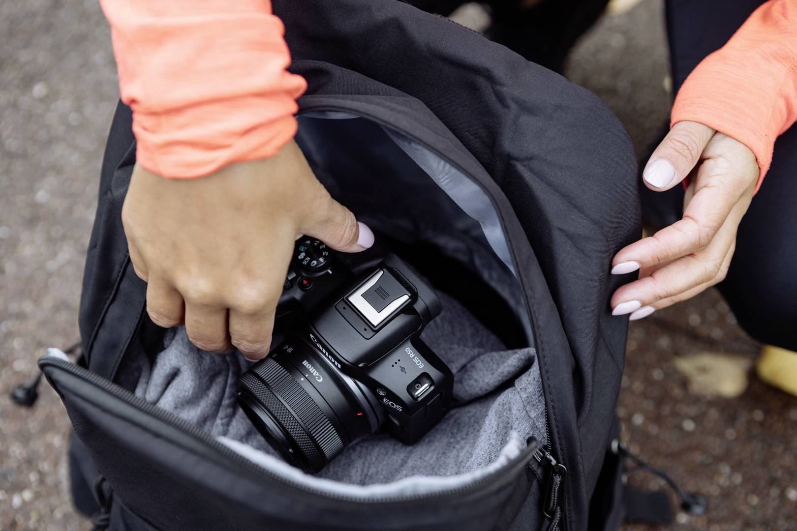 Une personne range un appareil photo noir dans un sac à dos noir. Des mains touchent l'appareil photo et la fermeture éclair du sac à dos.