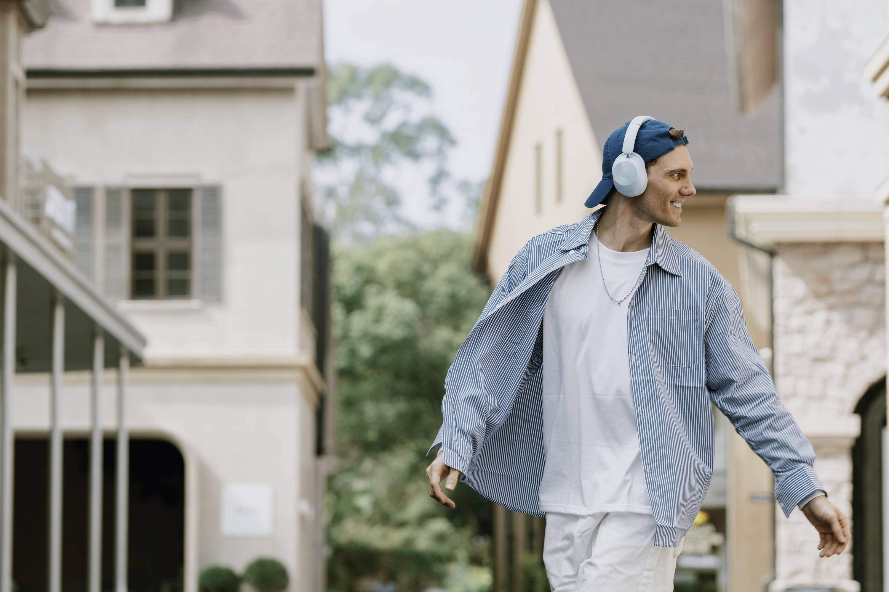 Une personne souriante porte des écouteurs et se promène tranquillement dans une rue pittoresque bordée de bâtiments historiques en arrière-plan.