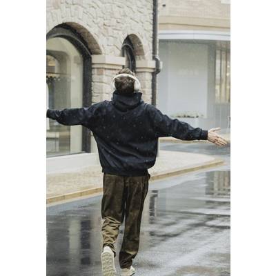 Une personne portant des écouteurs marche joyeusement sur une rue pavée humide, les bras grand ouverts, sous la pluie.