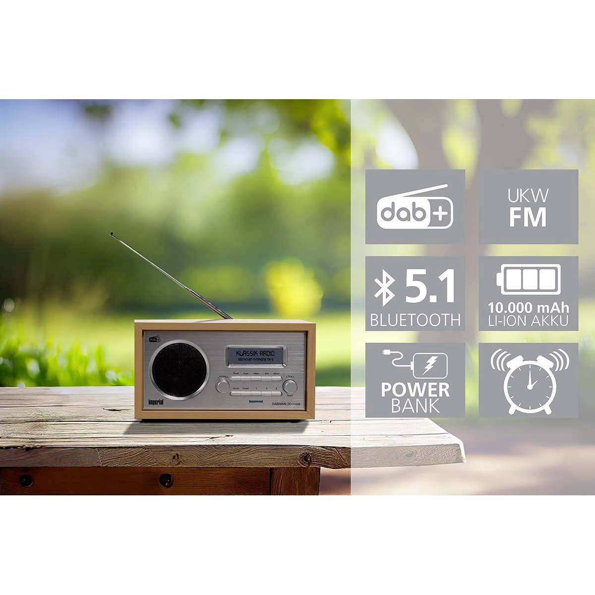 Radio vintage avec antenne posé sur une table en bois à l'extérieur. Symboles pour DAB+, FM VHF, Bluetooth 5.1, Powerbank, batterie Li-Ion 10 000 mAh.