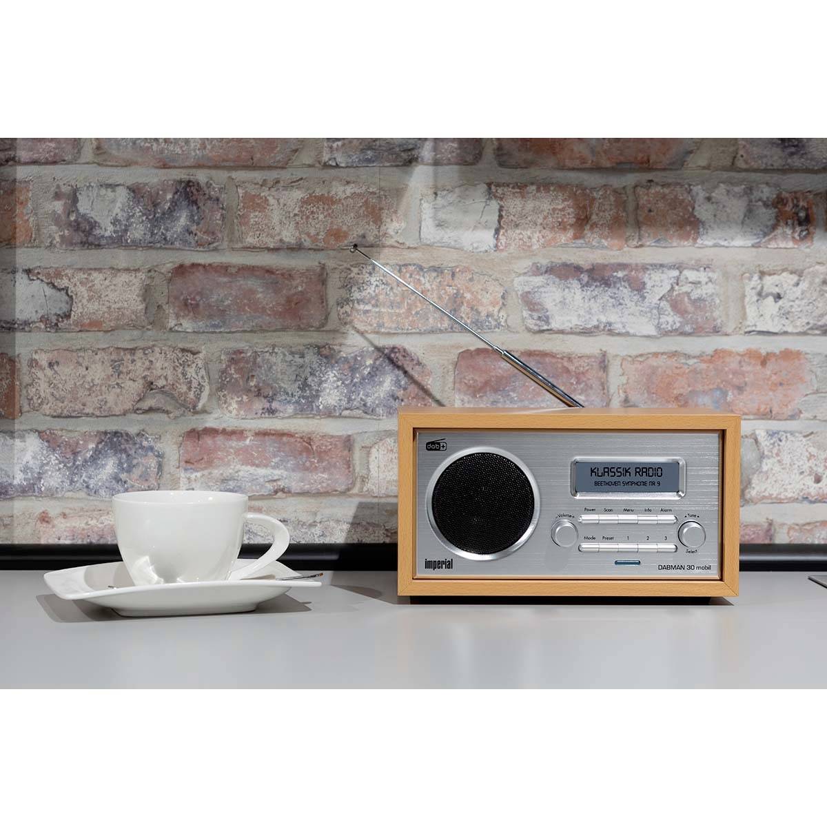 Un poste de radio classique est posé sur une table à côté d'une tasse blanche devant un mur de briques.