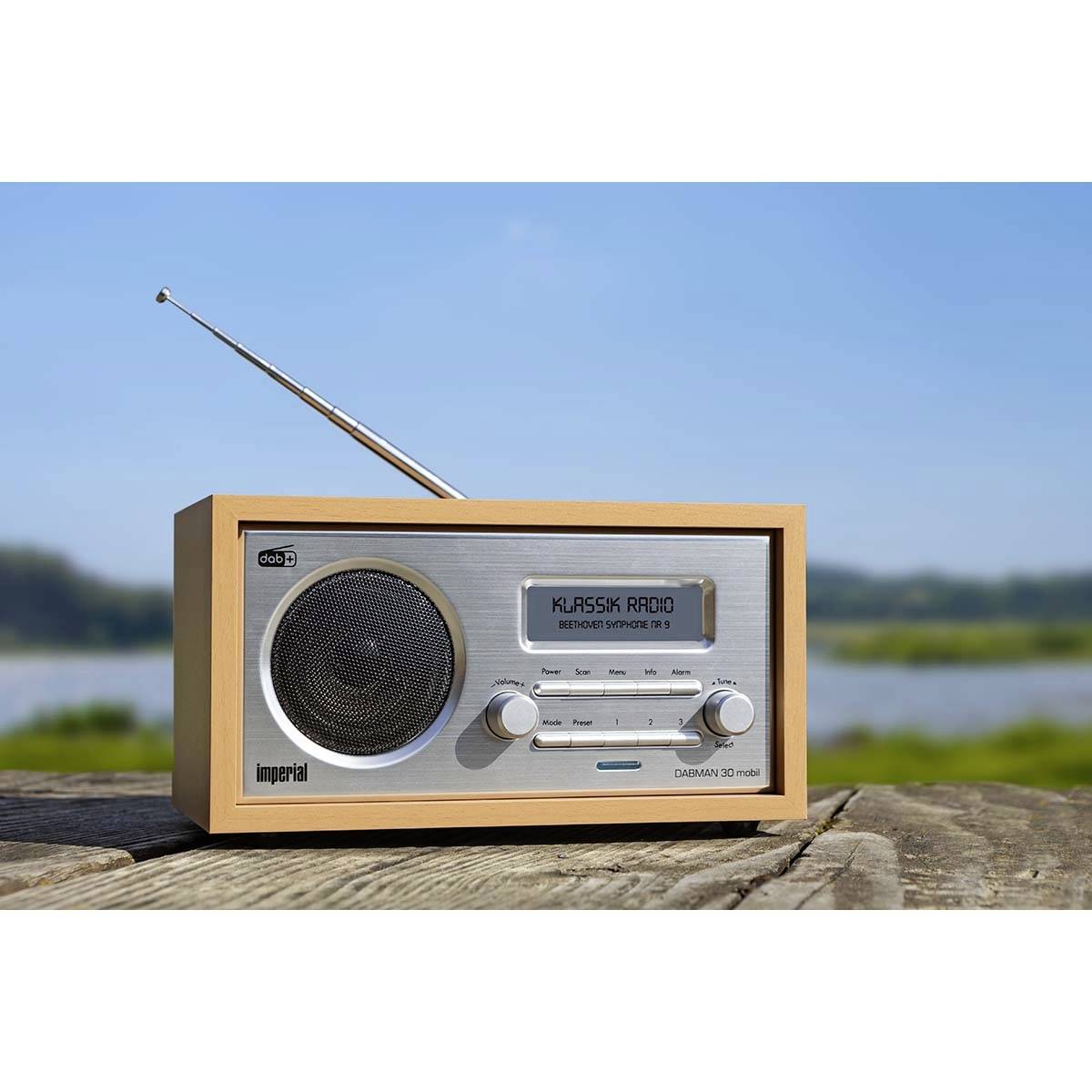 Un poste de radio rétro est posé sur une table en bois devant un paysage naturel. L'écran affiche 'Klassik Radio'.