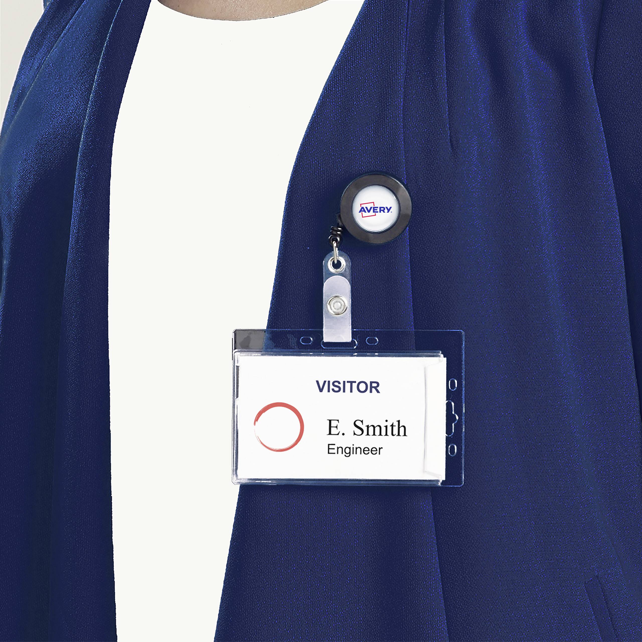 Une personne porte un badge nominatif sur lequel est inscrit 'Visitor' et 'E. Smith, Ingénieur'. Elle porte un haut bleu.