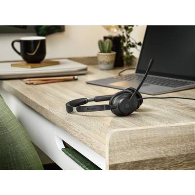 Un espace de travail avec un ordinateur portable et un casque sur un bureau. Des livres et des plantes sont visibles en arrière-plan.
