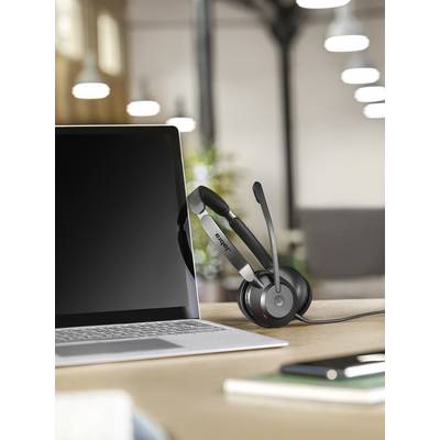 Un ordinateur portable posé sur un bureau avec un casque audio suspendu. Des meubles et un éclairage de bureau flous en arrière-plan.