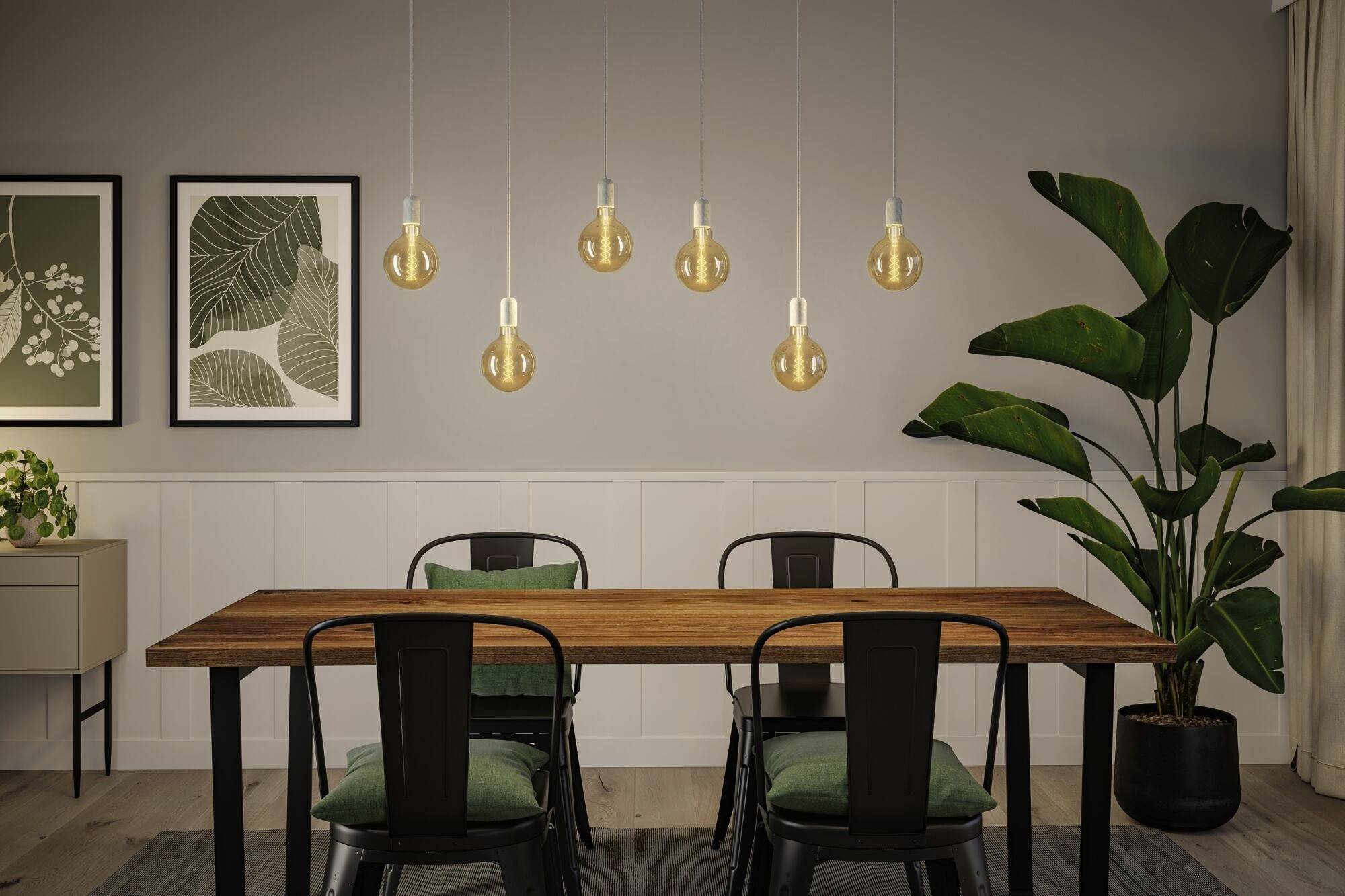 Salle à manger avec une table en bois et quatre chaises. Deux images botaniques encadrées sont accrochées au mur. Une plante d'intérieur est placée à droite.