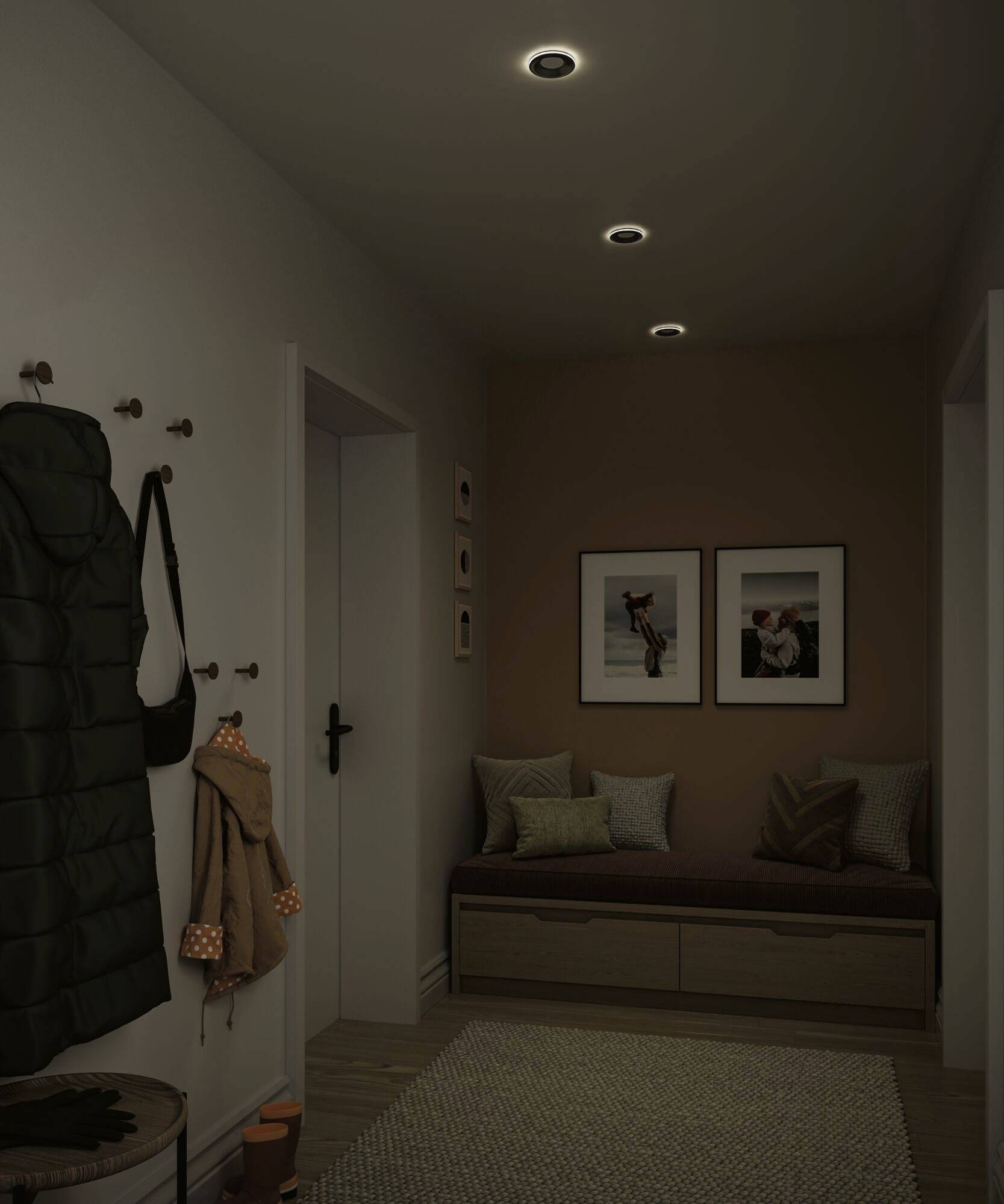 Un couloir chaleureux avec des lumières de plafond tamisées. Des photos sont accrochées au mur ; des coussins sont posés sur le banc. Des manteaux et un sac sont suspendus aux crochets.