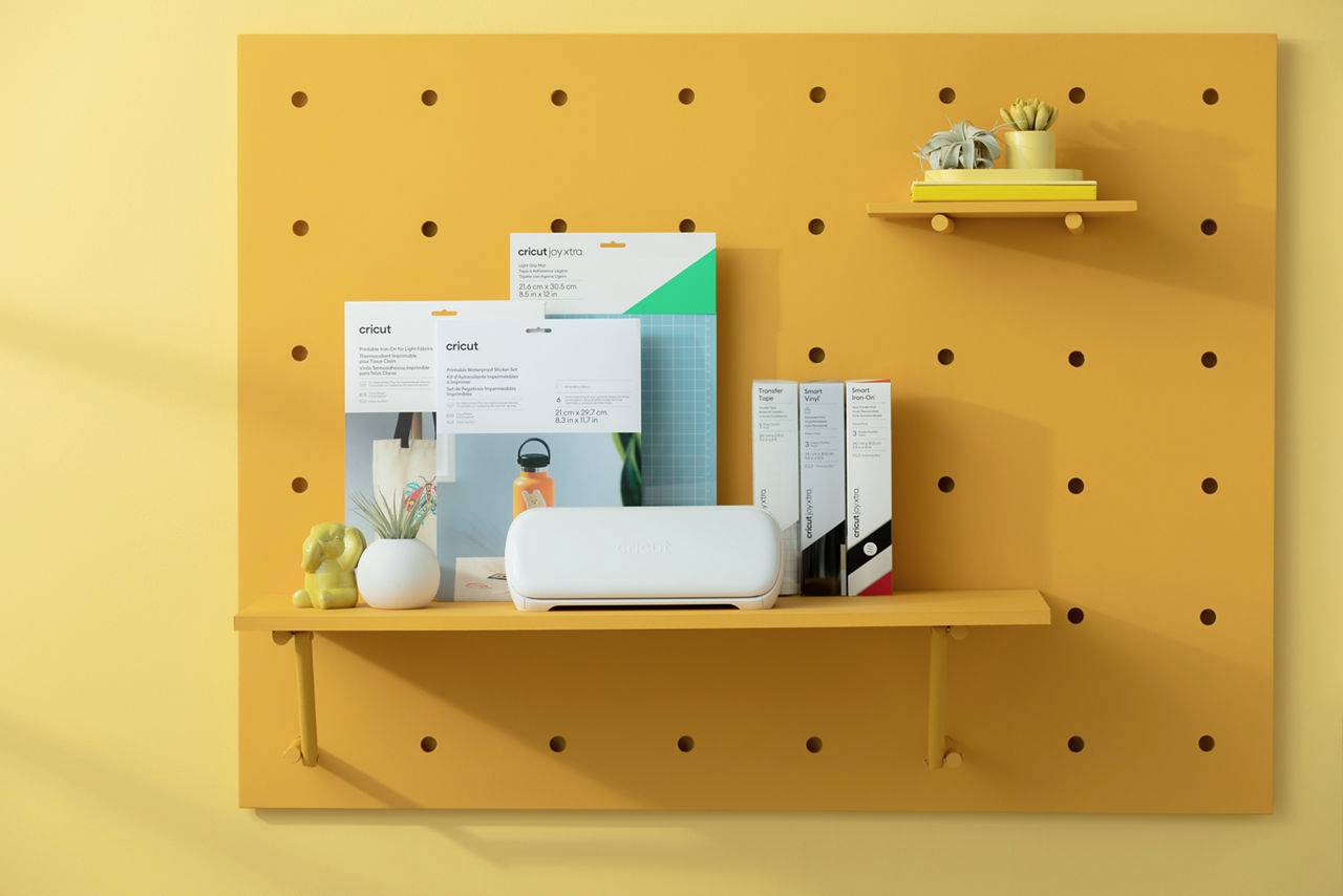 Coin créatif avec une étagère jaune présentant une plante, des emballages d'accessoires artistiques et un appareil blanc.