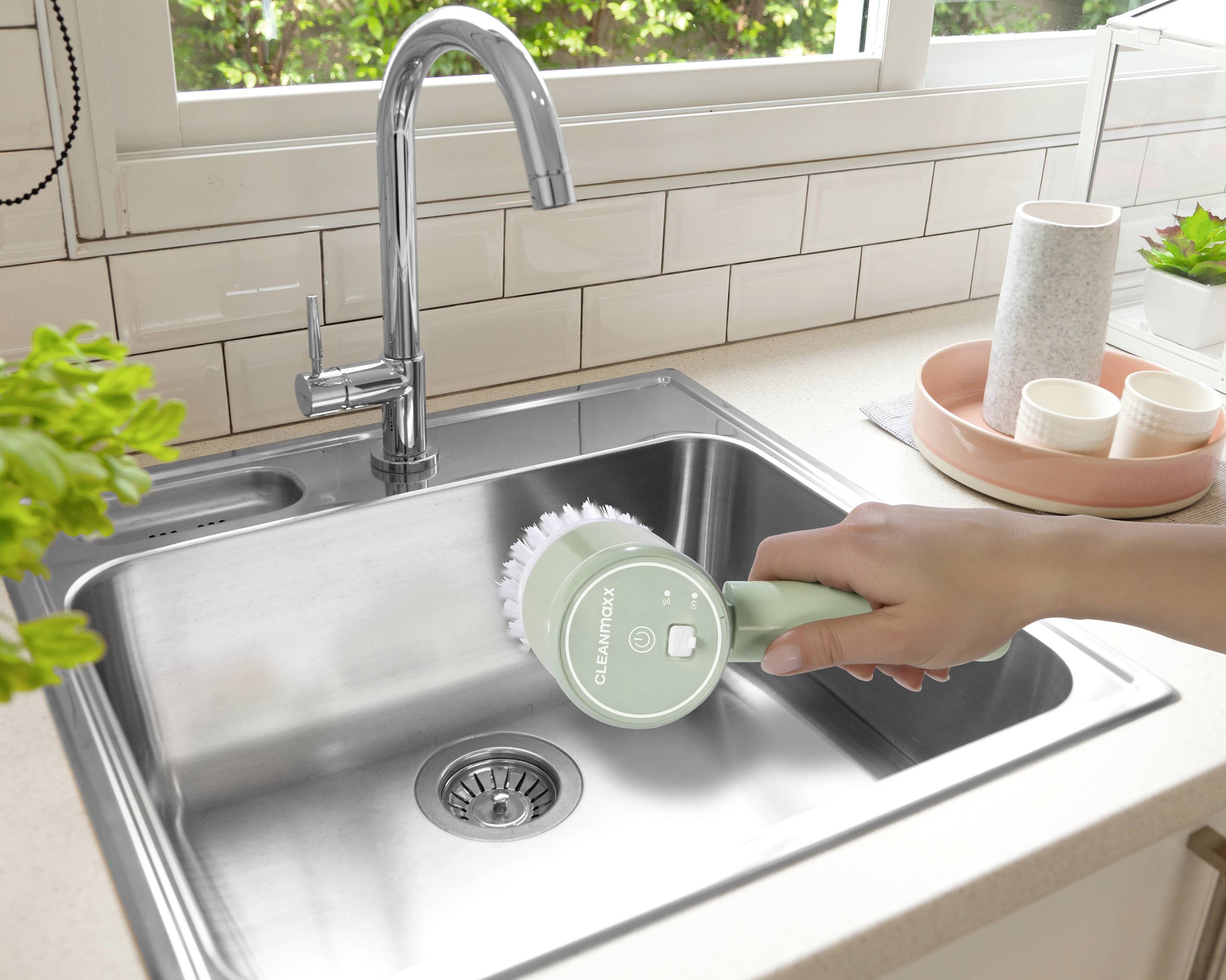 Une personne nettoie un plan de travail de cuisine avec un appareil de nettoyage électrique. Une cuisine moderne est visible en arrière-plan.