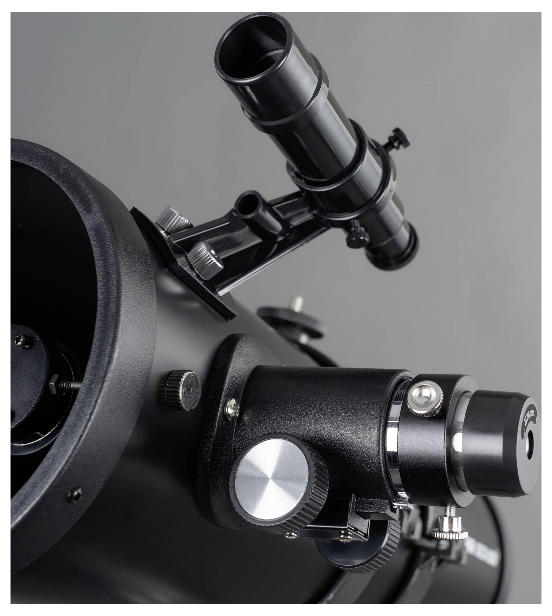 Un télescope noir avec viseur, boutons de réglage et vue sur le miroir principal sur un fond gris.