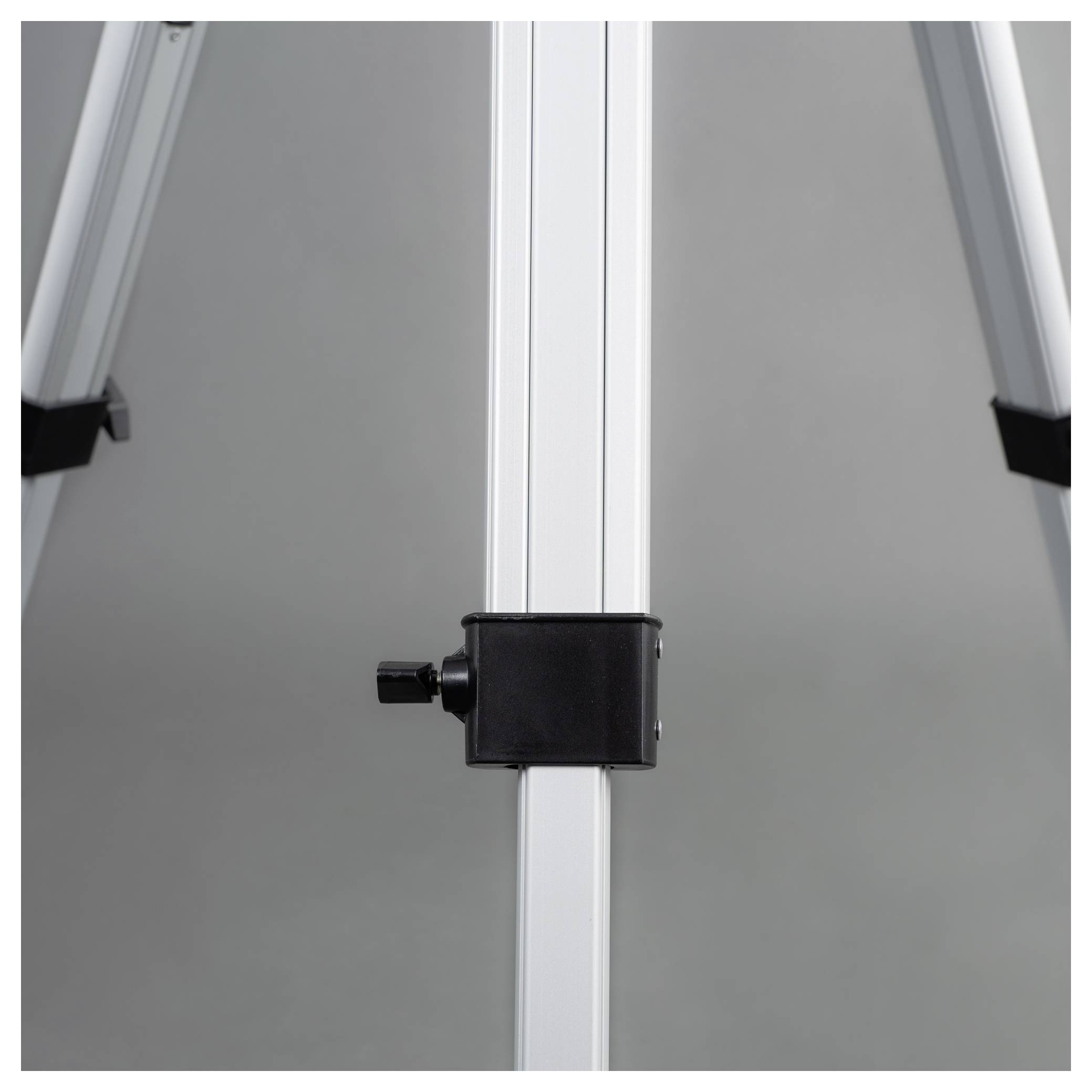 Un trépied en métal argenté avec un mécanisme de verrouillage réglable, monté sur un support noir, sur un fond gris.