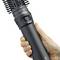 Une main tient une brosse à cheveux noire avec sèche-cheveux intégré.