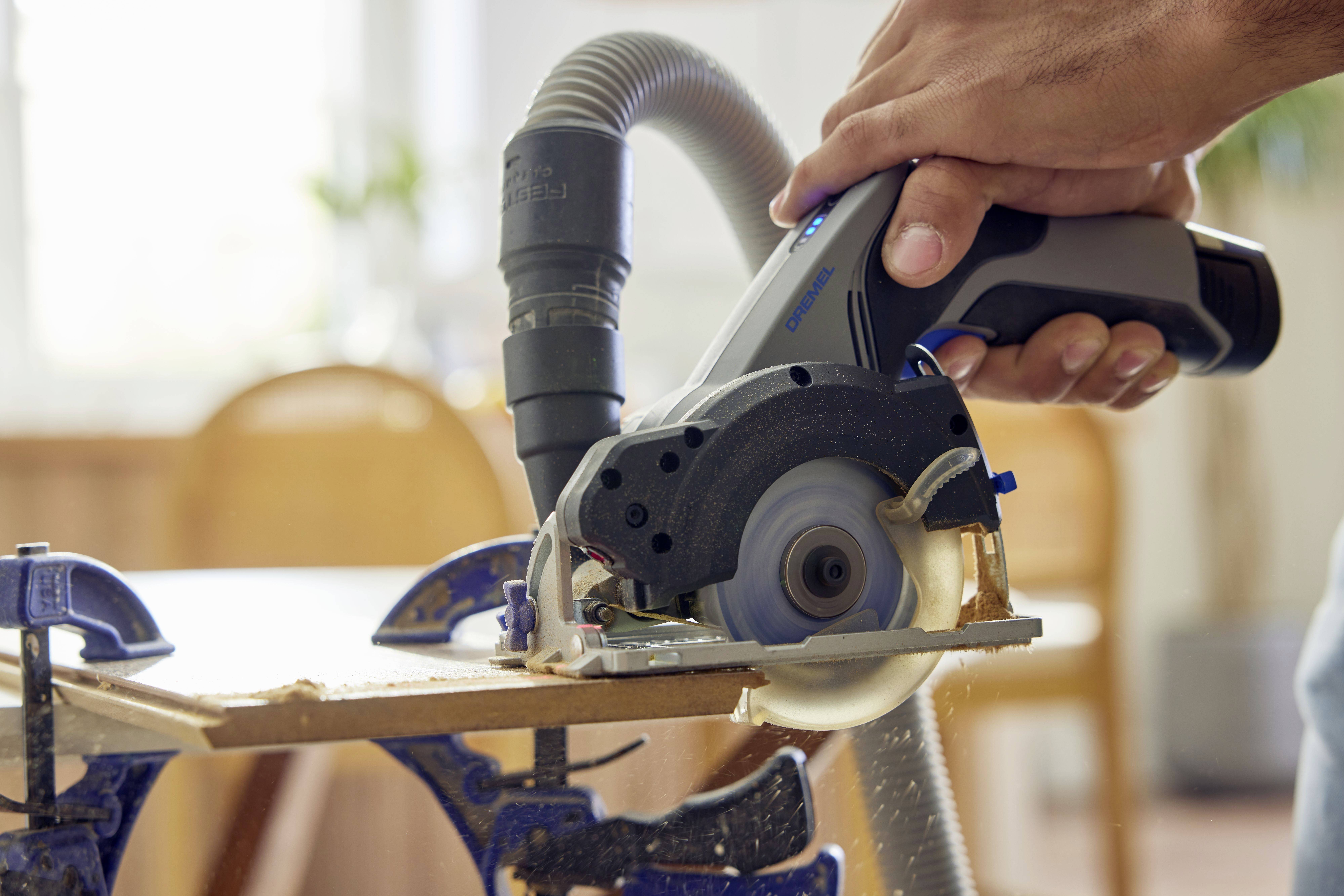 Gros plan d'une main utilisant une scie circulaire à main sur une planche de bois fixée à une table à l'aide de serre-joints.