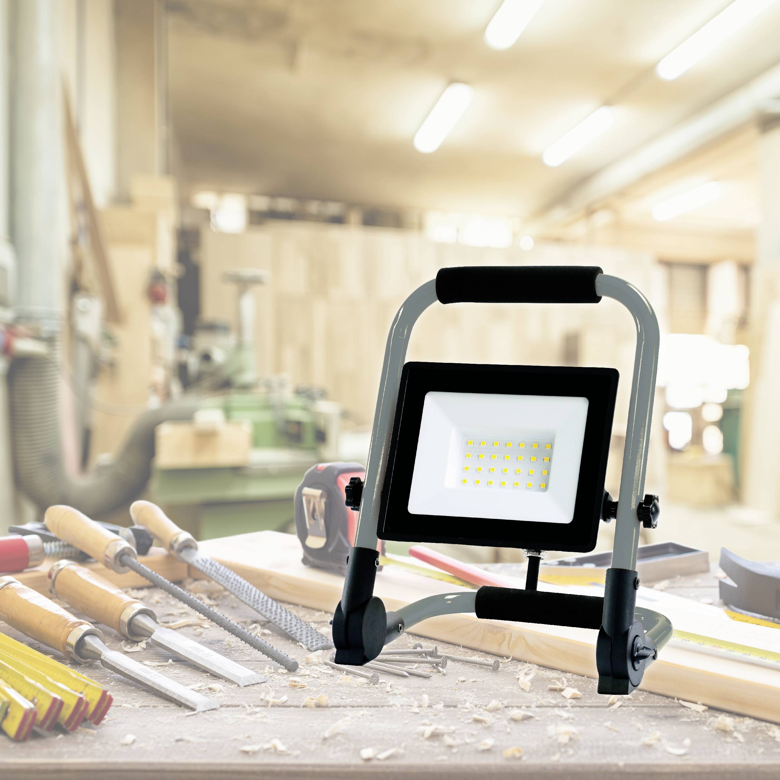 Un atelier avec un outil électrique sur un établi. Au premier plan, divers outils manuels, à l'arrière-plan des machines floues.