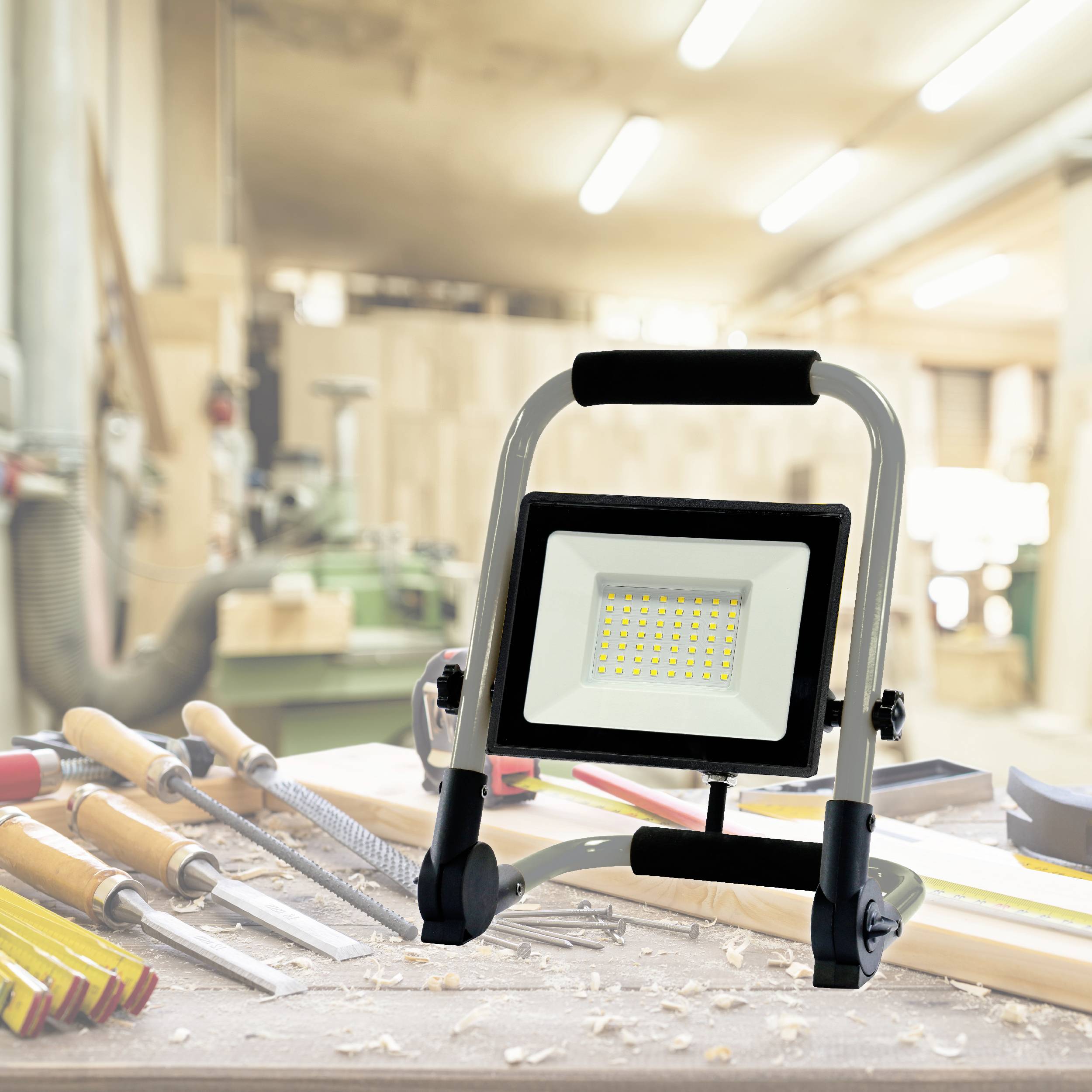 Photo d'atelier : Lampe de travail LED portable posée sur un établi, entourée de divers outils à main dans une menuiserie.