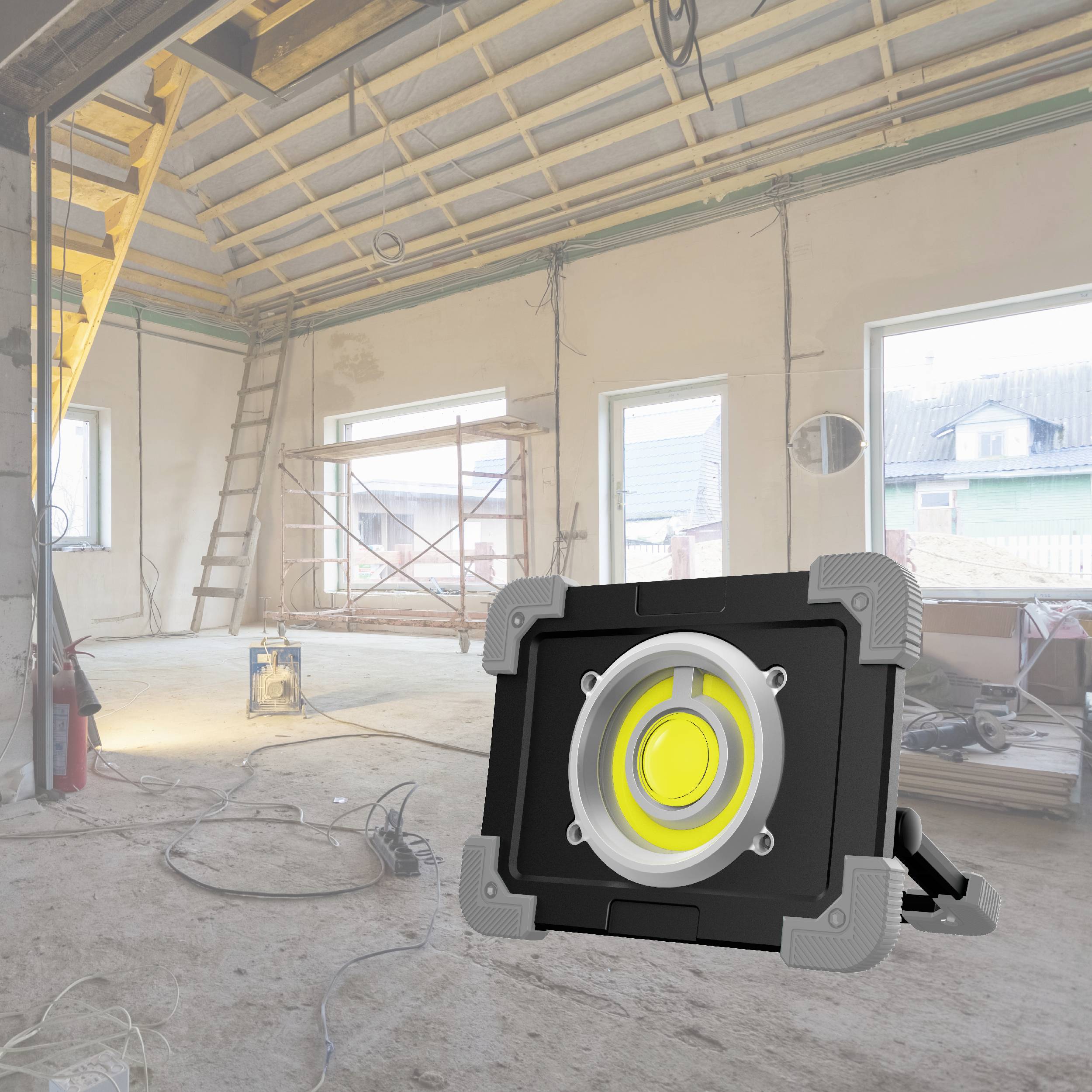 Sur un chantier avec des murs inachevés, un projecteur de chantier est au premier plan. Des échelles et des échafaudages sont également visibles.