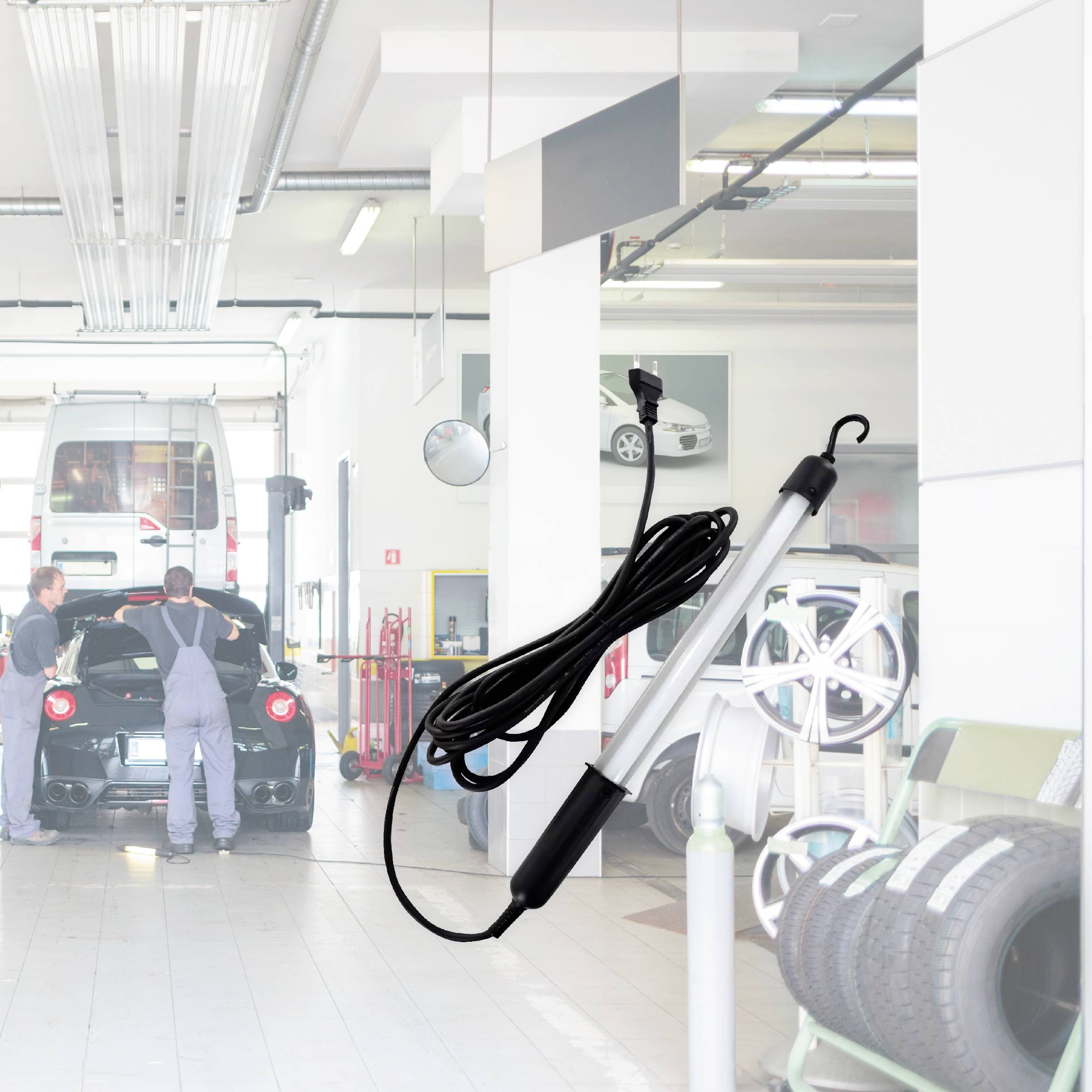 Deux mécaniciens travaillent sur une voiture de sport rouge dans un atelier automobile. Des pneus de voiture et des outils sont visibles au premier plan.