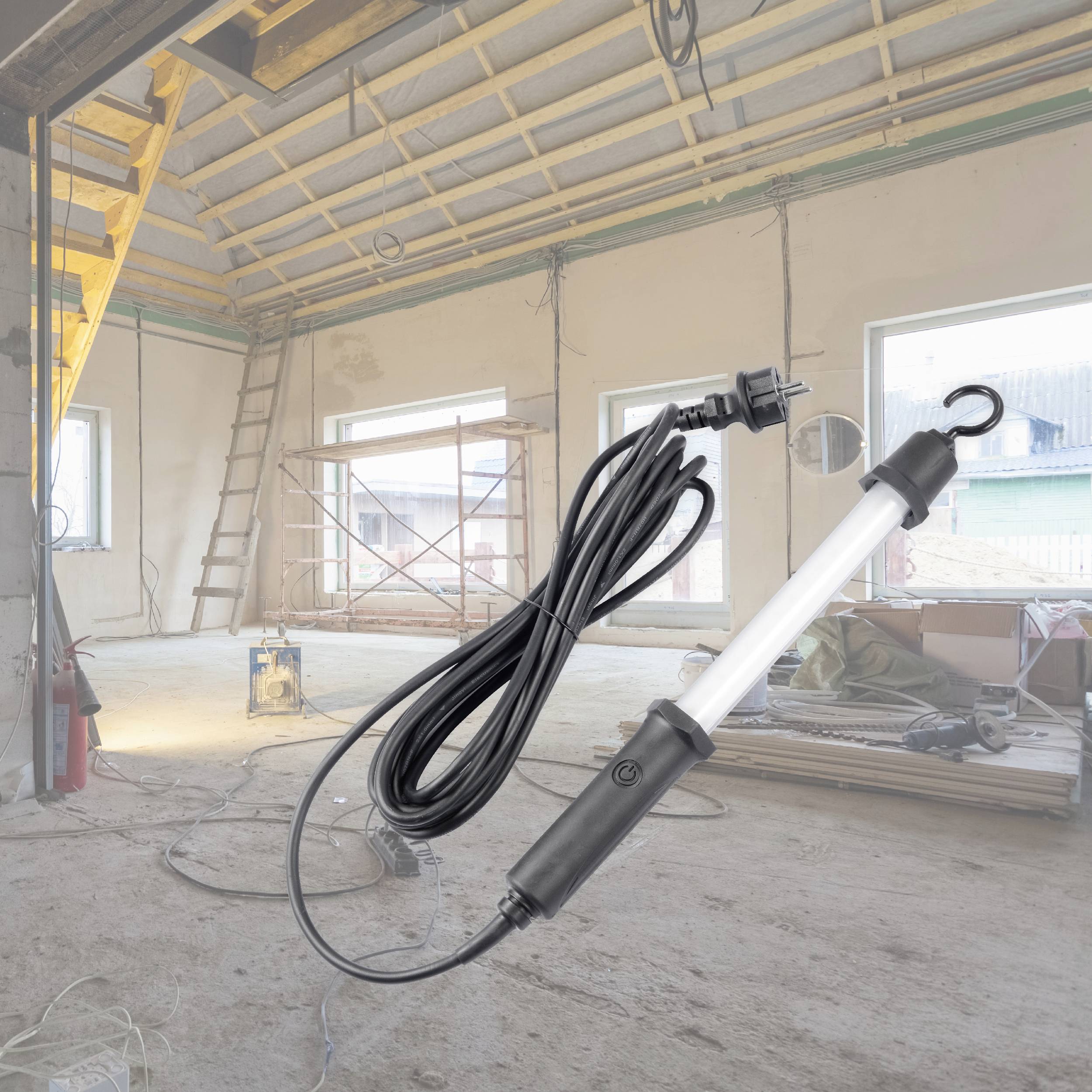 Un chantier avec des échafaudages et des matériaux de construction dans l'espace. Une lampe de travail avec un long câble est posée au premier plan.
