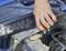 Une main utilise des pinces pour tordre des fils sous le capot d'une voiture, effectuant des travaux de maintenance ou de réparation sur les composants du moteur.