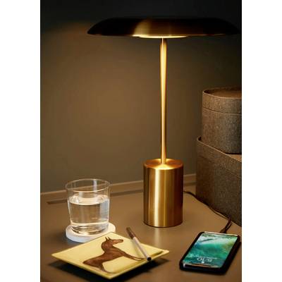 Une lampe de table dorée s'illumine sur une table à côté d'un verre d'eau, d'un bloc-notes à motif de cheval et d'un smartphone.
