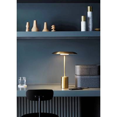 Un bureau élégant avec une table moderne, sur laquelle se trouve une lampe dorée et une bouteille d'eau. Des étagères en arrière-plan sont décorées avec des objets décoratifs.