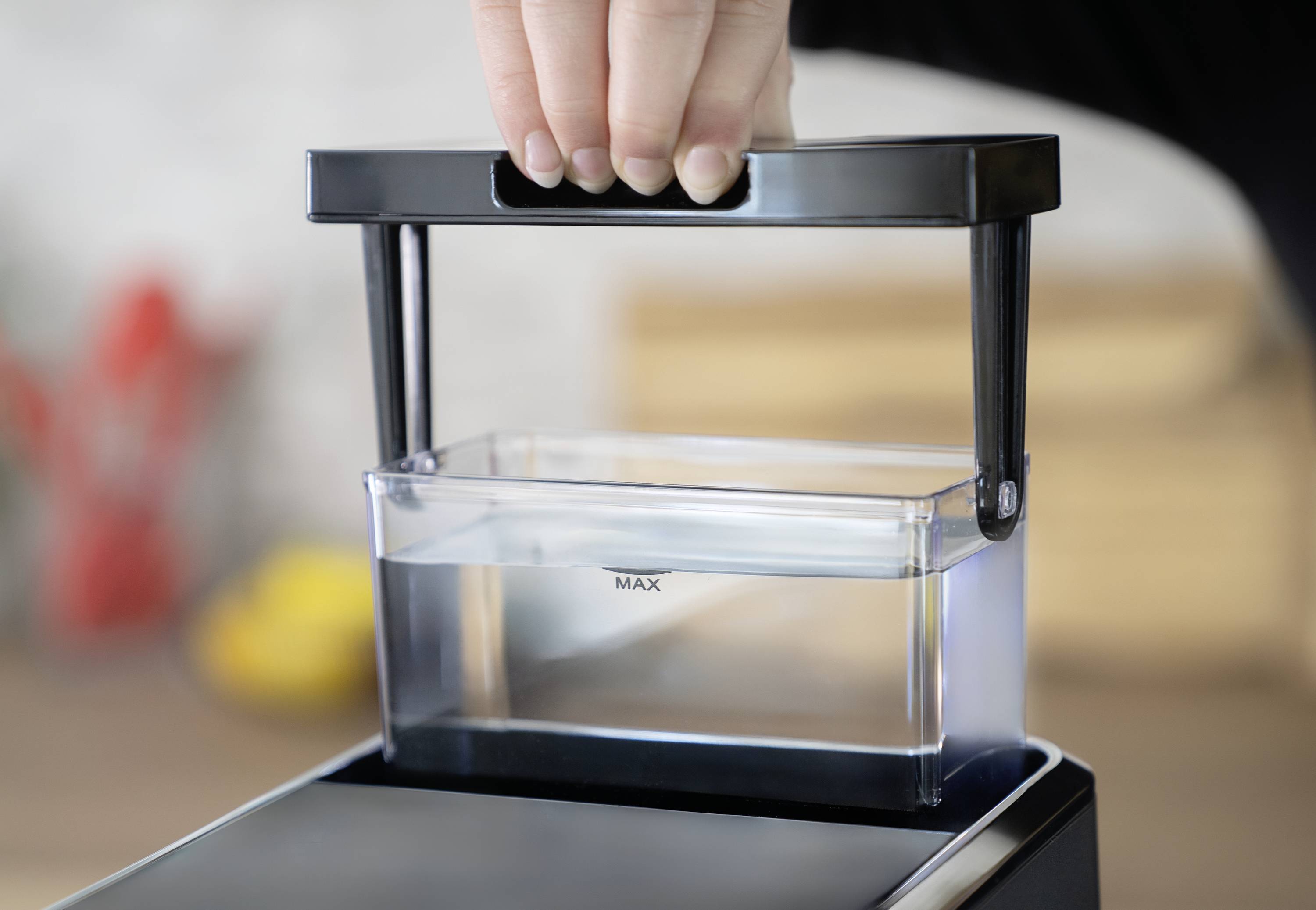 Une main soulève un réservoir d'eau d'une machine. Le réservoir d'eau indique la marque 'MAX' pour le remplissage maximum.