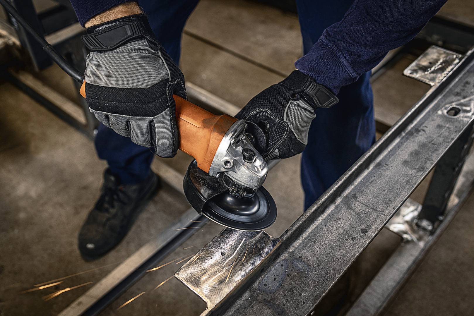 Une personne porte un équipement de protection et meule du métal avec une meuleuse d'angle. Des étincelles volent de la surface travaillée.