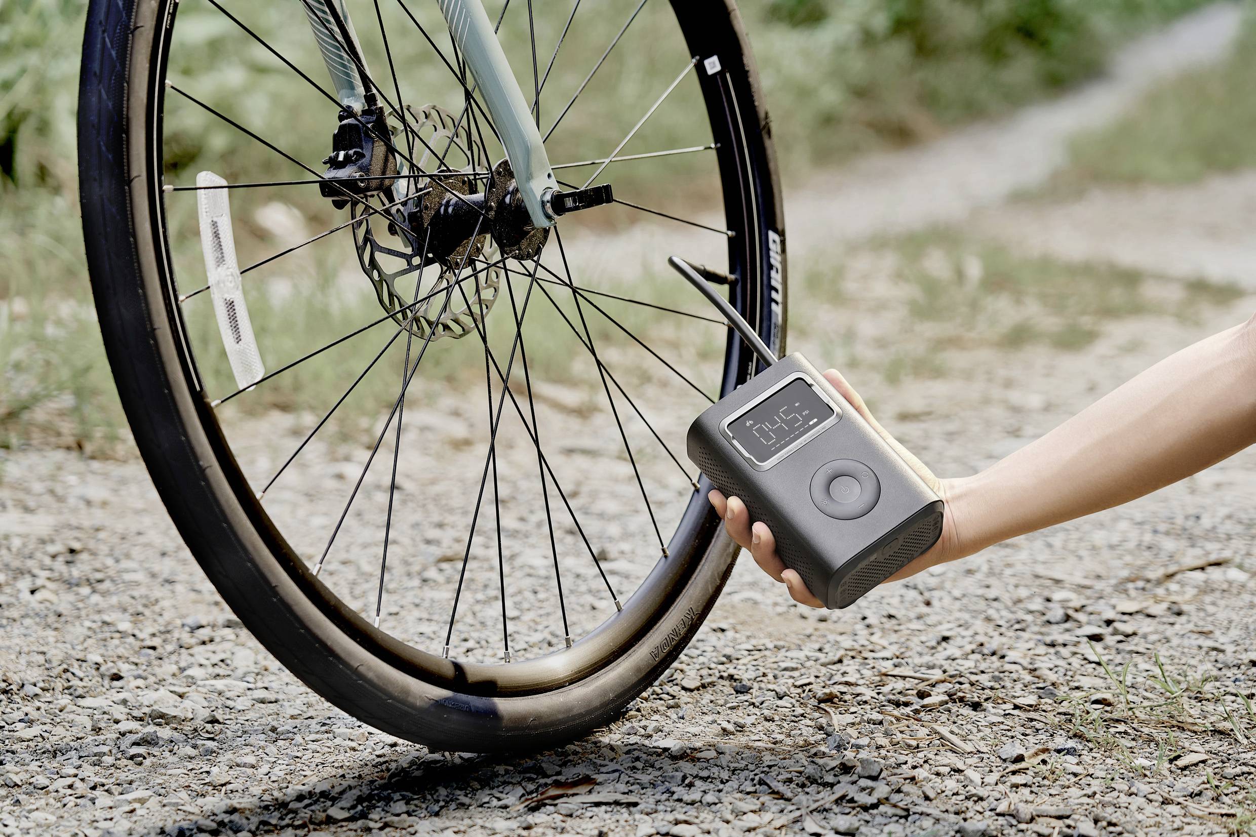 Une main utilise une pompe à air portable pour gonfler le pneu d'un vélo sur un chemin de gravier.